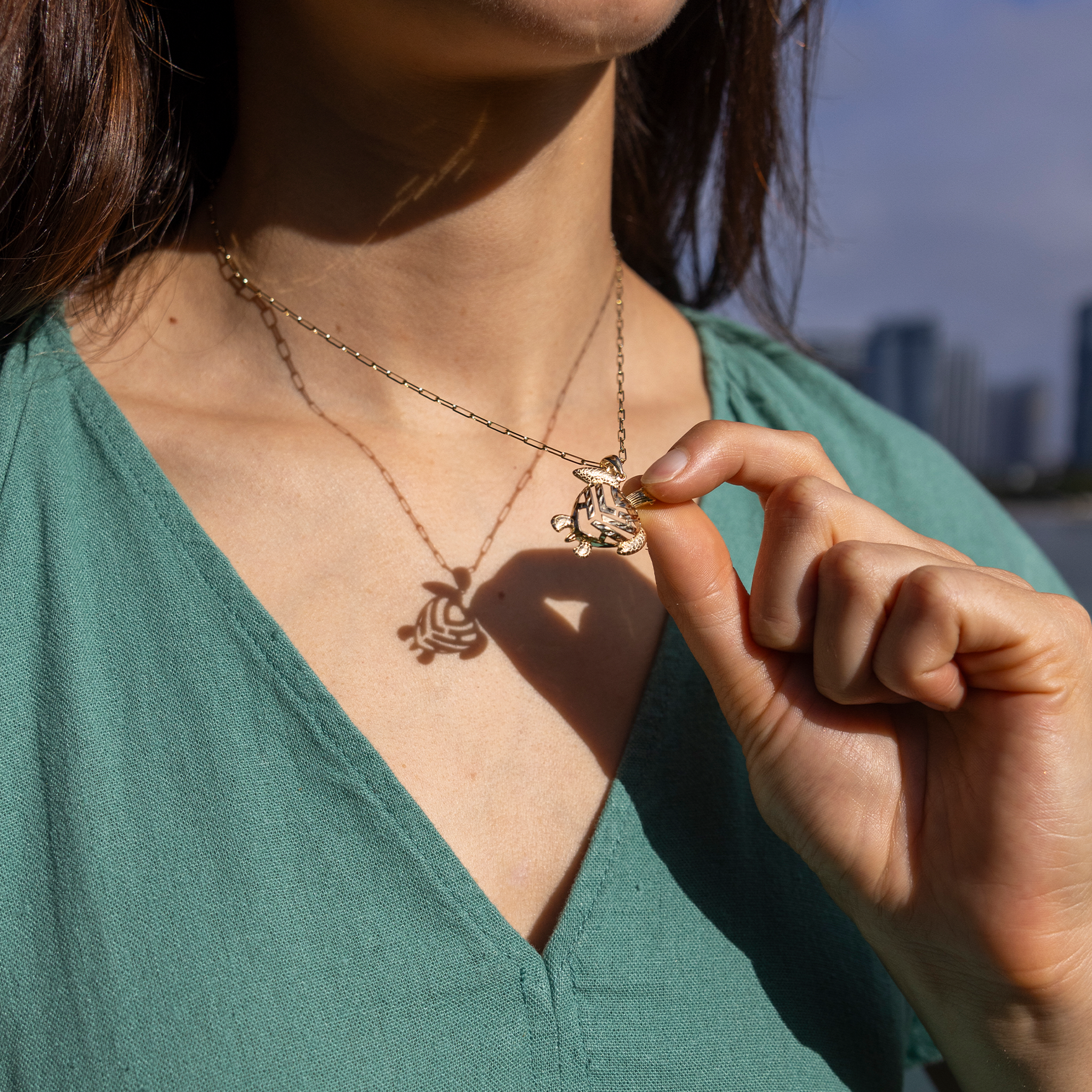 Woman wearing a Honu Aloha Heart Pendant in Gold, holding it to cast shadow that reads Aloha