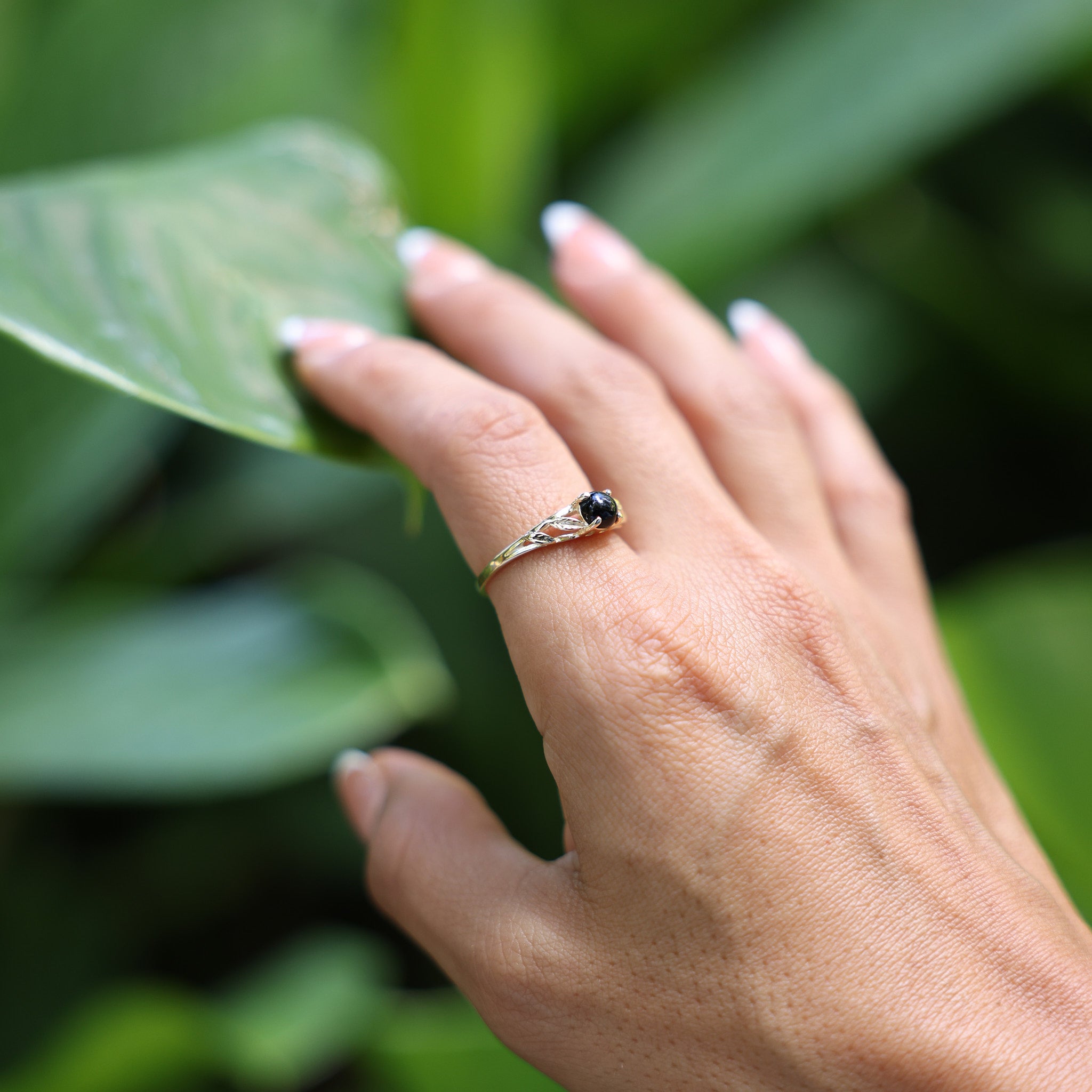Woman wearing Maile Leaf Hawaiian Black Coral Ring in Gold with leafy background
