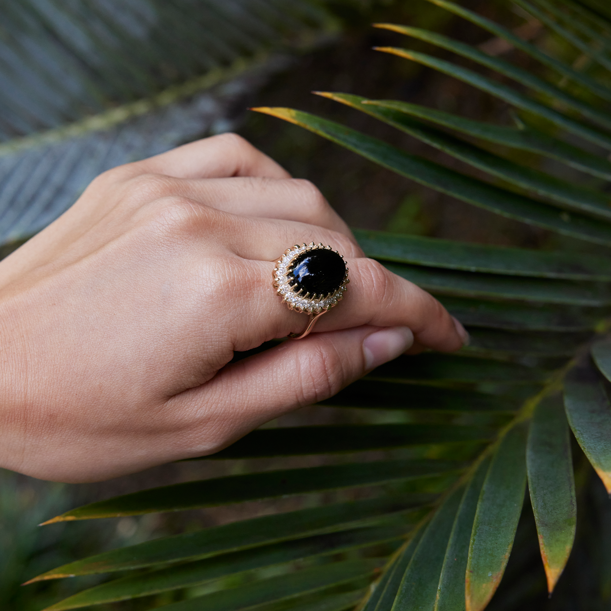 Hand against leaf wearing a Princess Ka‘iulani Hawaiian Black Coral Ring in Gold with Diamonds