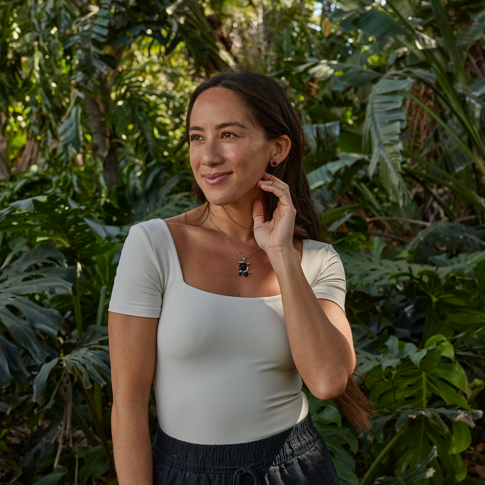 Woman in tropical garden wearing a Honu Mom & two babies Black Coral Pendant in white gold