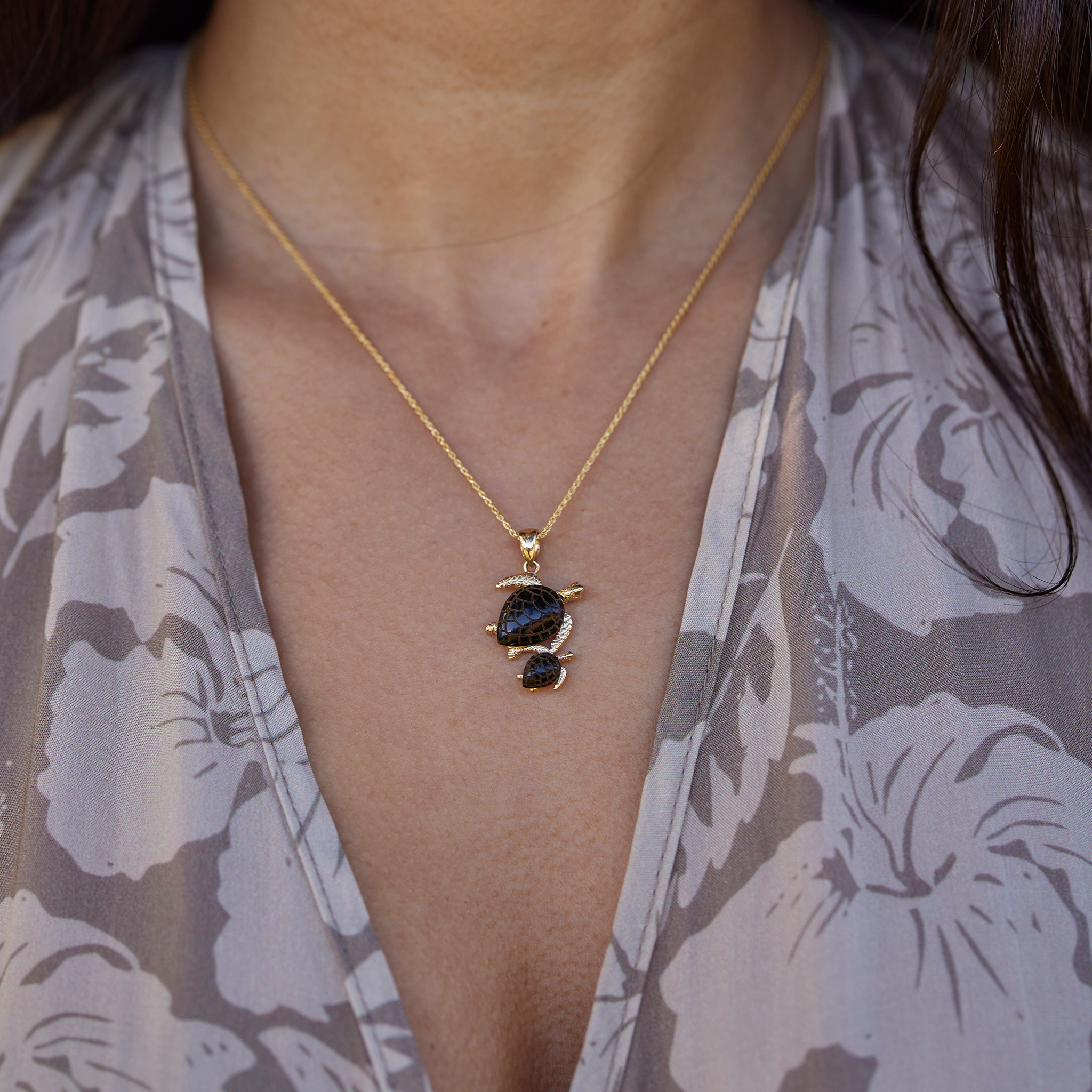 Close up of a person wearing a Honu Mom & Baby Black Coral Pendant in 14k Yellow Gold
