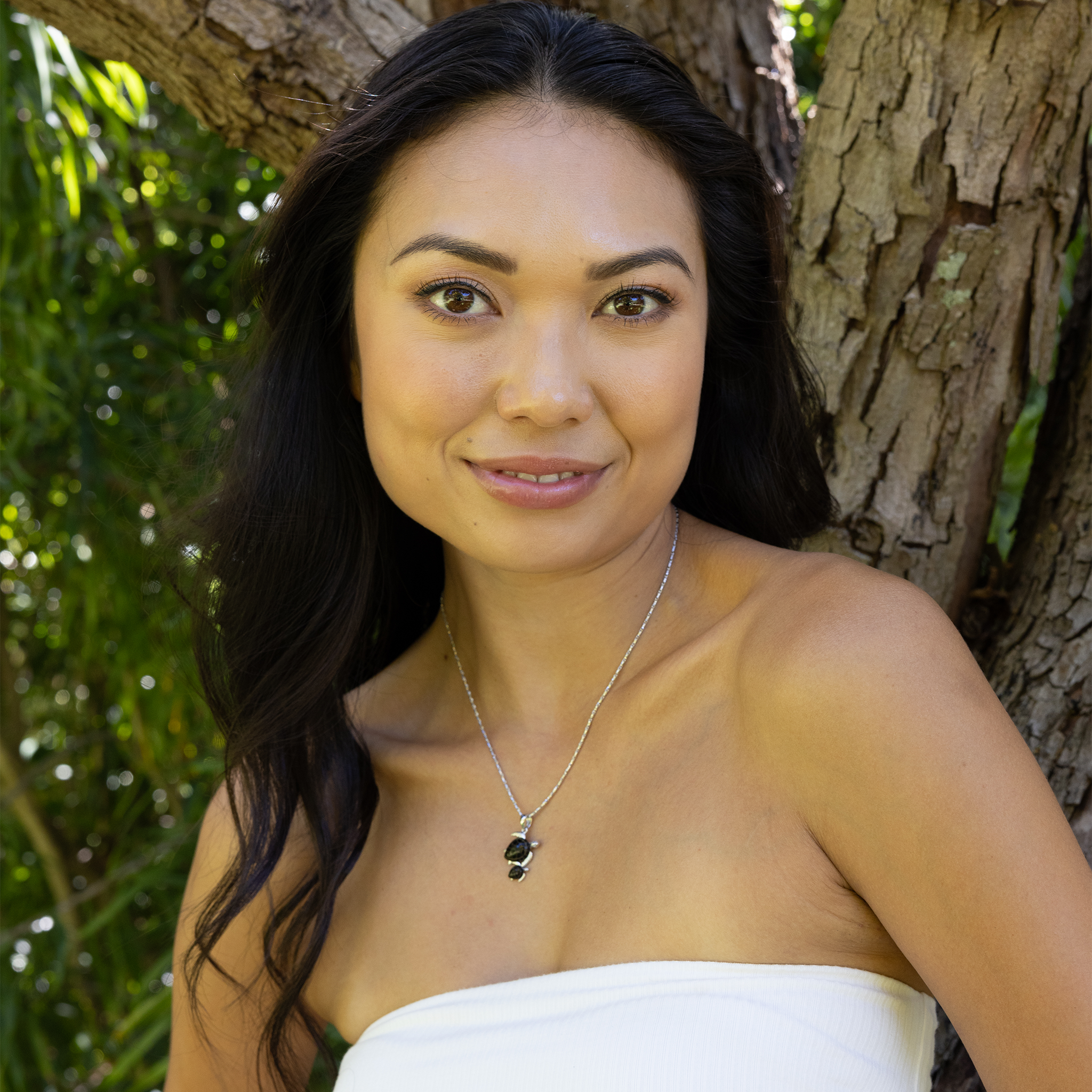 Woman standing in front of a tree wearing Honu Mom & Baby Black Coral Pendant in White Gold