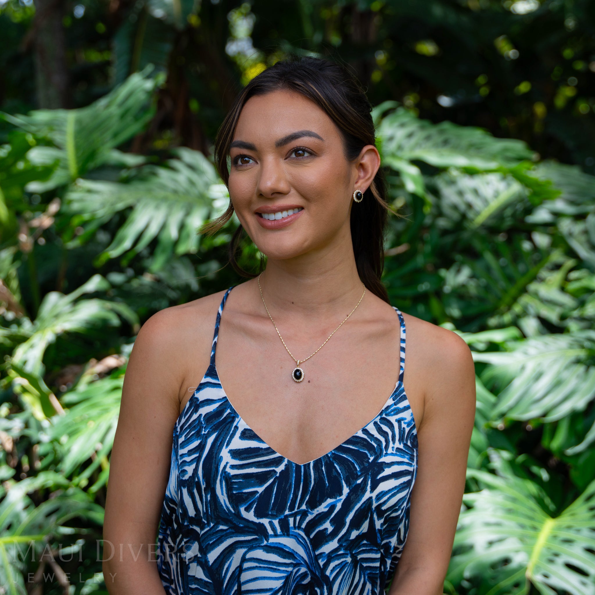Woman in a tropical garden wearing a Princess Ka‘iulani Black Coral Pendant and earring in Gold with Diamonds