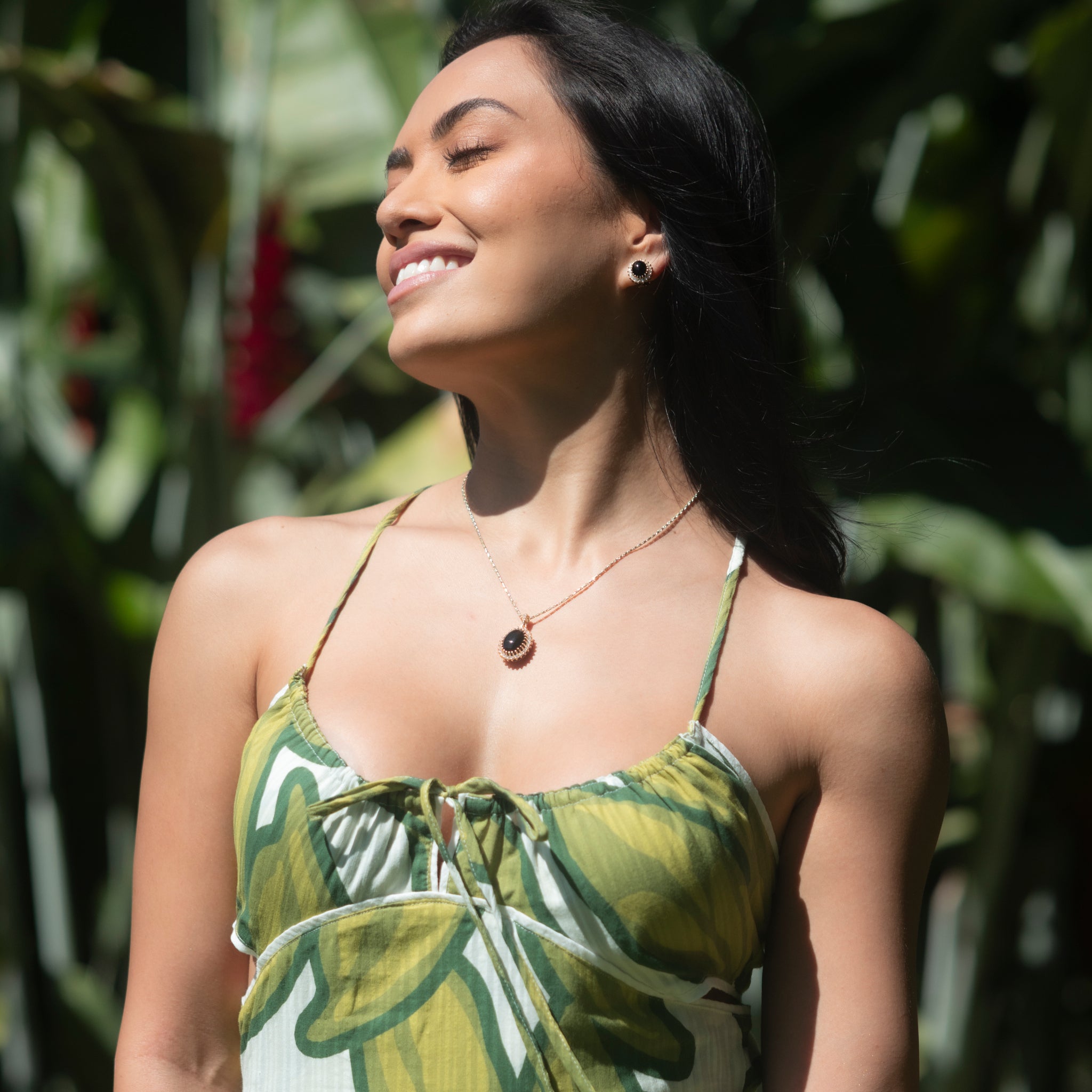 Woman in tropical garden wearing Princess Ka‘iulani Black Coral Pendant and earrings in Gold with Diamonds