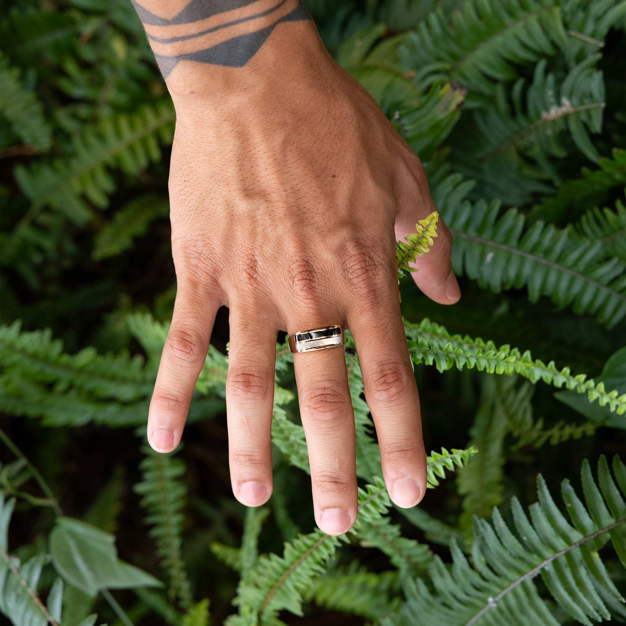 Hand above fern background wearing Black Coral Ring in Gold with Mother of Pearl