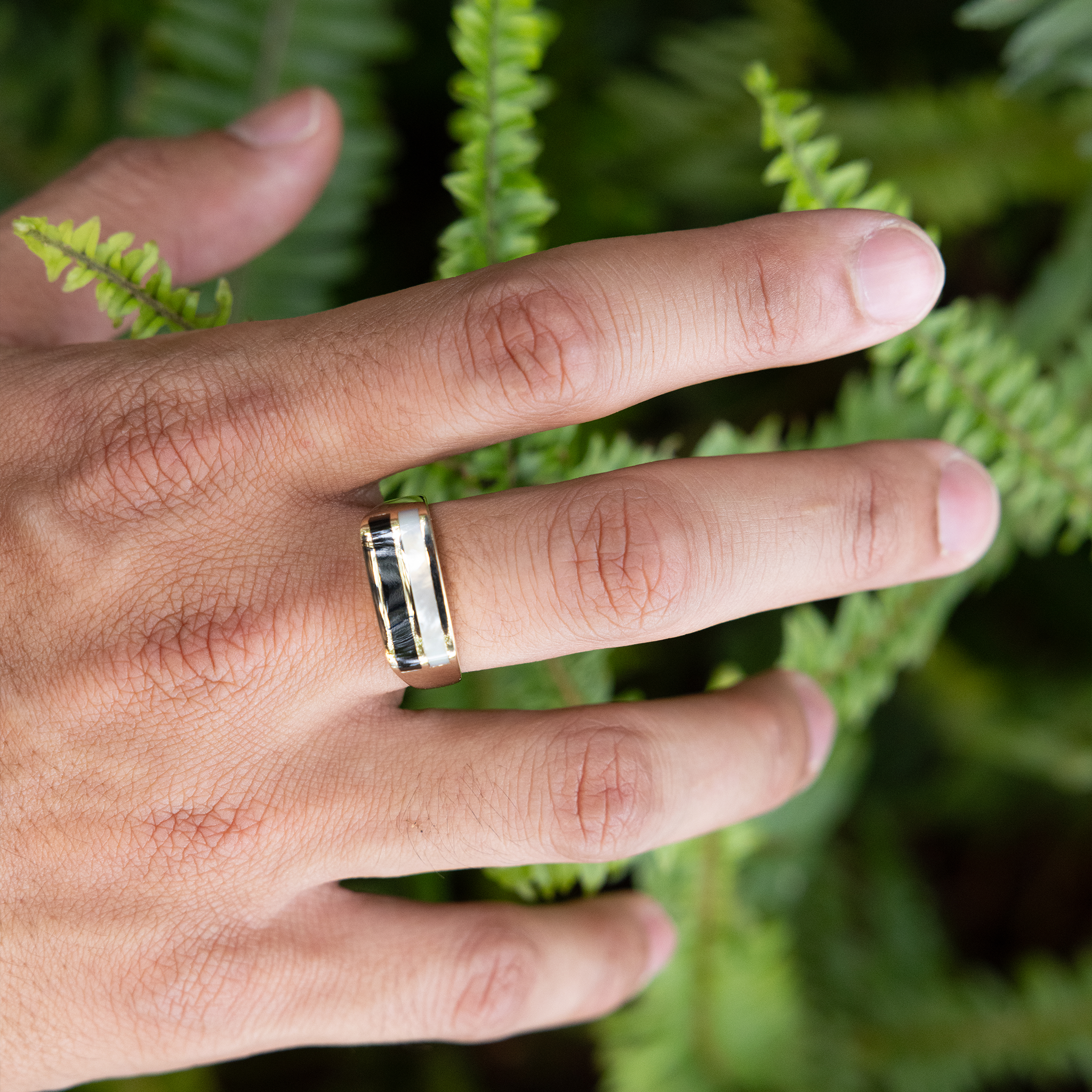 Hand over fern background wearing Black Coral Ring in Gold with Mother of Pearl
