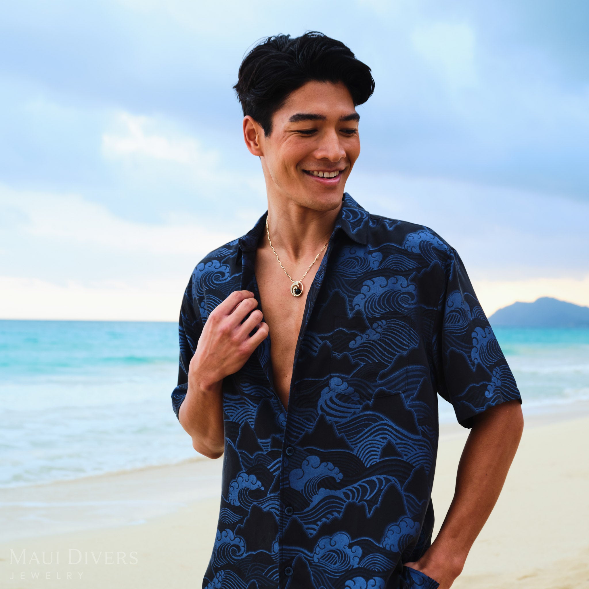 Man wearing a Nalu Black Coral Pendant in Gold with Diamonds on a beach