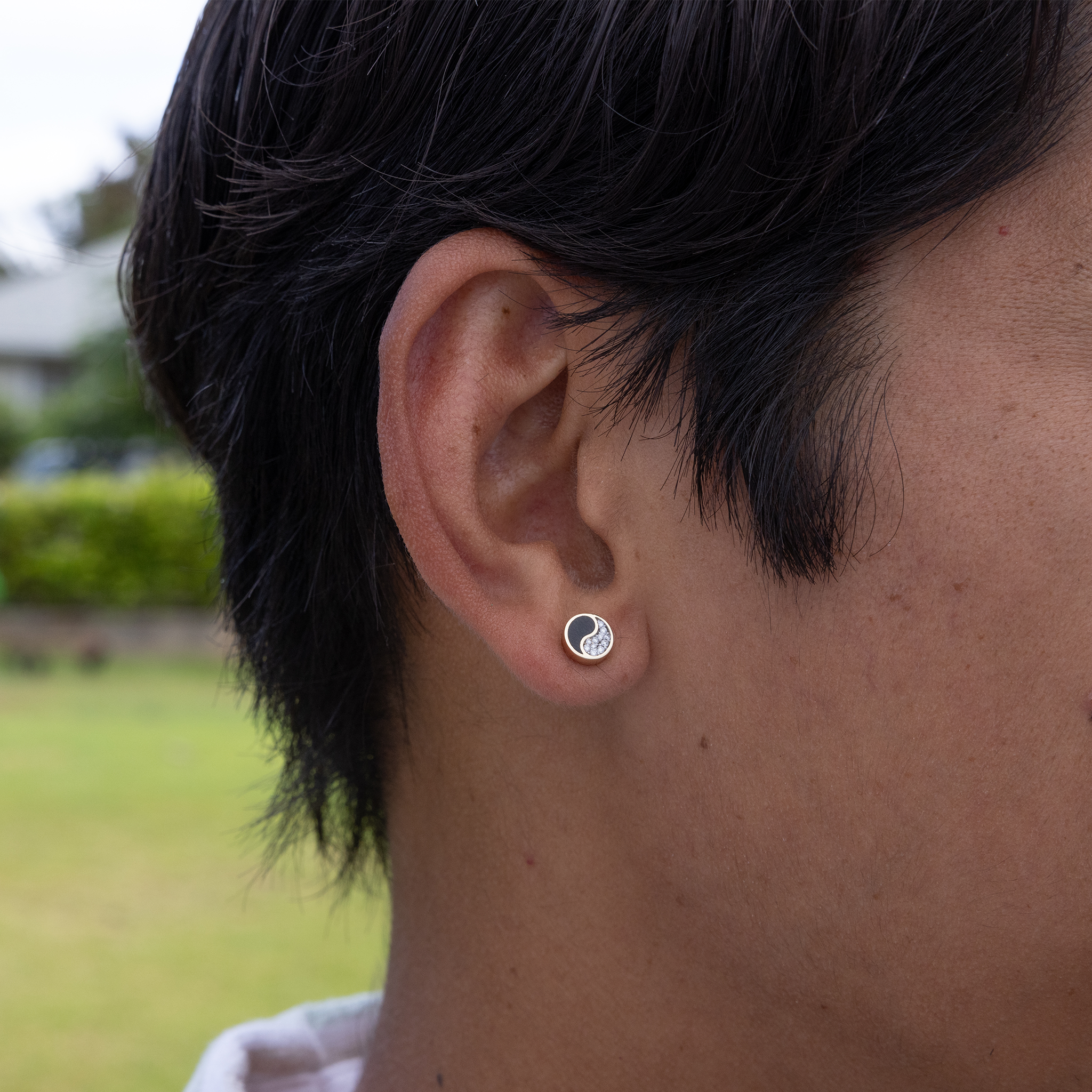 Close up of man's ear wearing Yin Yang Black Coral stud Earrings in Gold with Diamonds