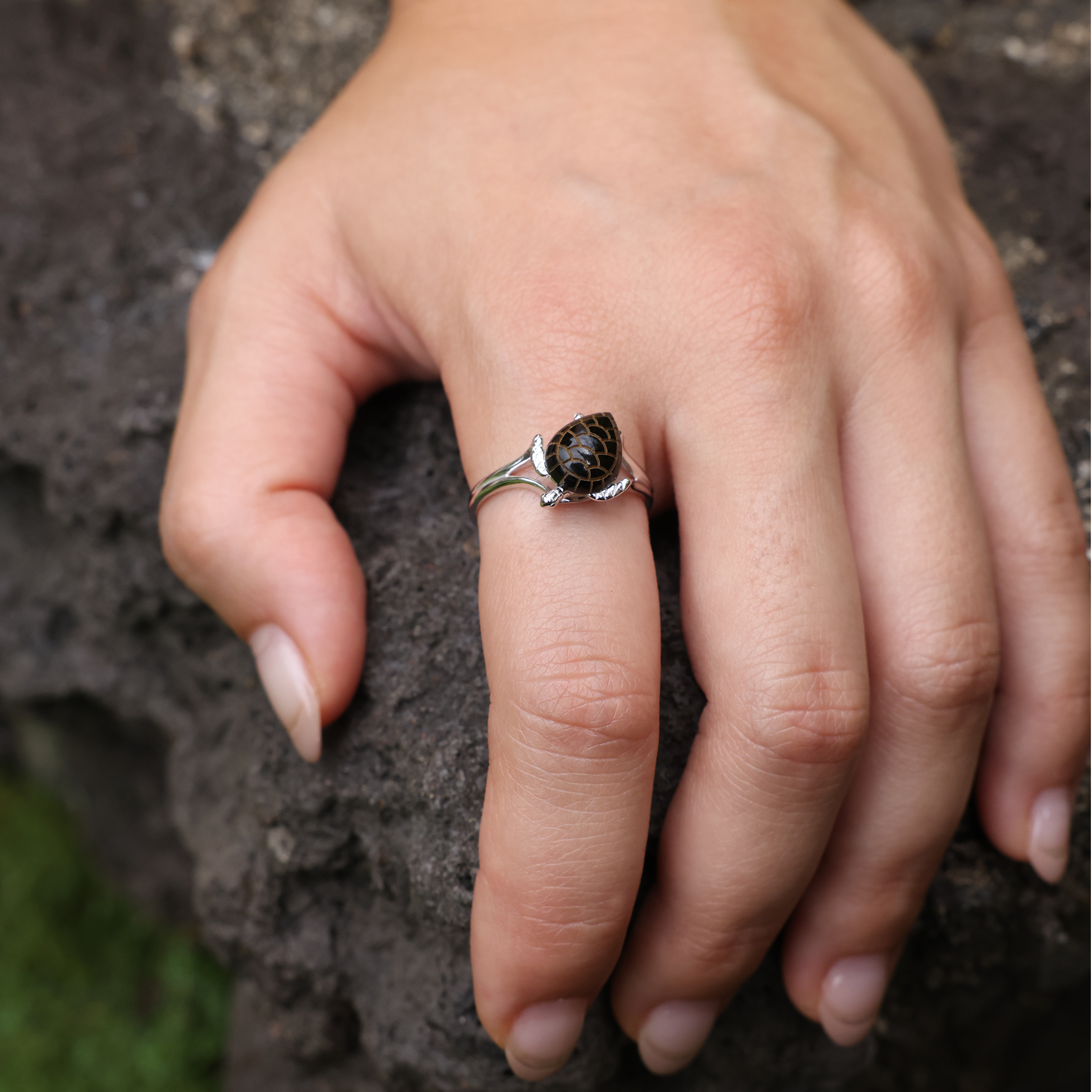 Hand on a rock wearing Honu Black Coral Ring in White Gold