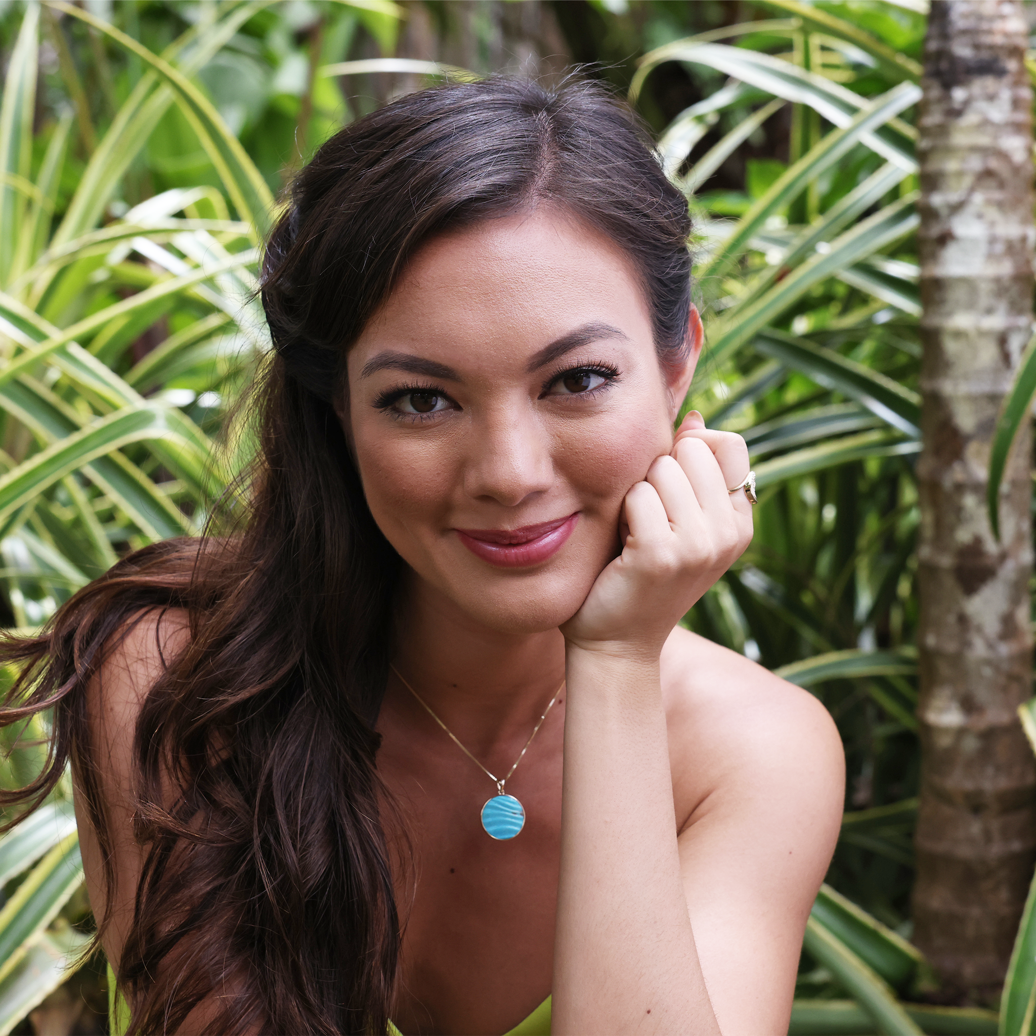 A woman wearing a Hawaiian Moments Ocean Sand Pendant in Gold with Turquoise holding her head - Maui Divers Jewelry