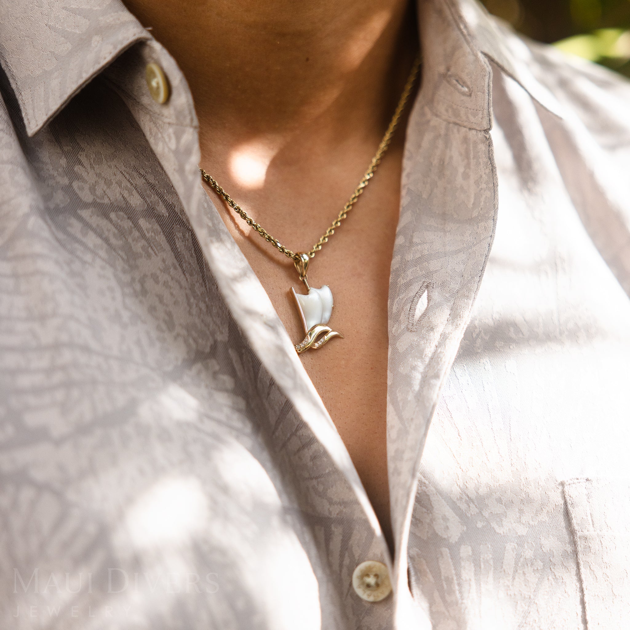 Waʻa (canoe) Mother of Pearl Pendant in Gold with Diamonds worn by a person in a light shirt.