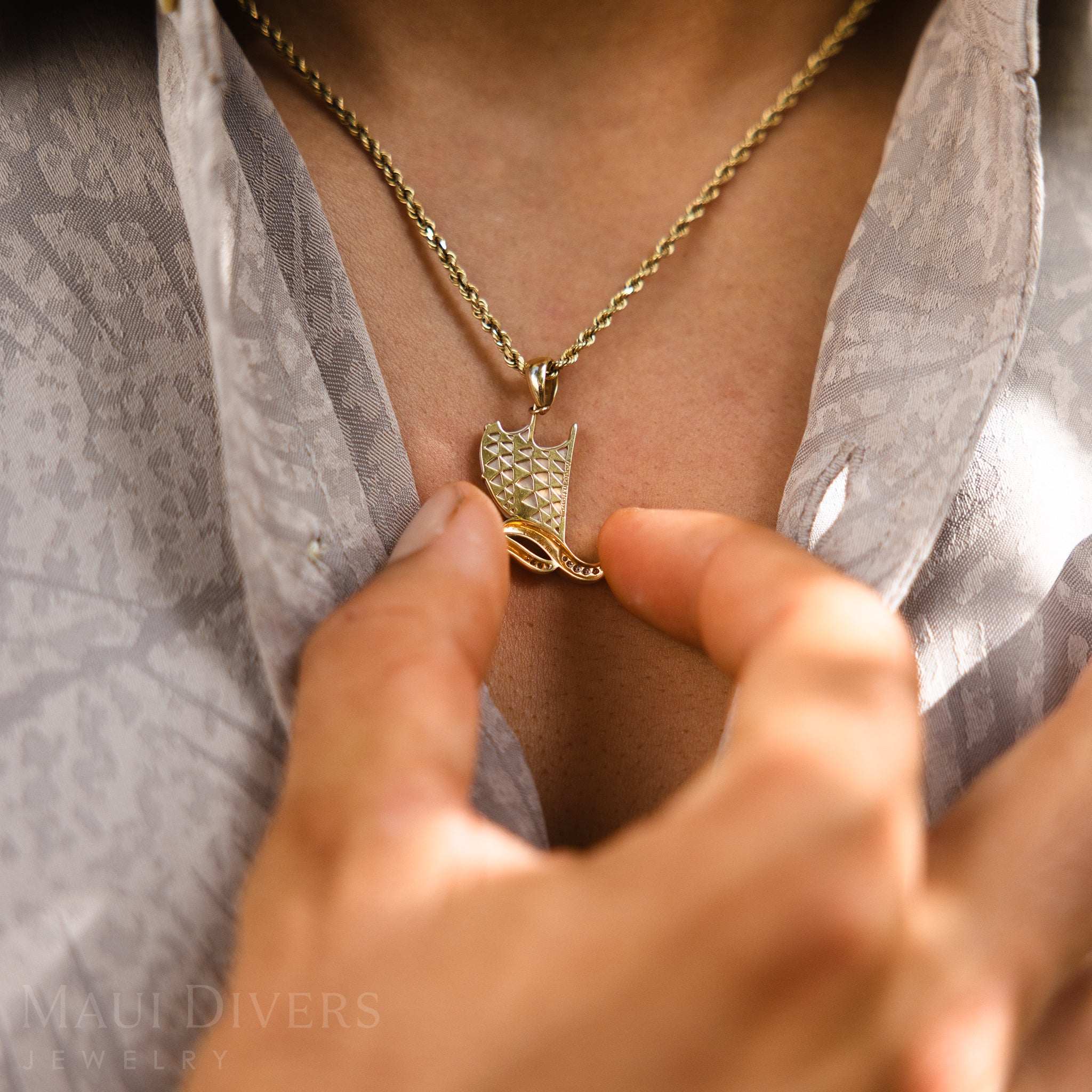 Backside gold detail of Waʻa (canoe) pendant on man with light colored shirt