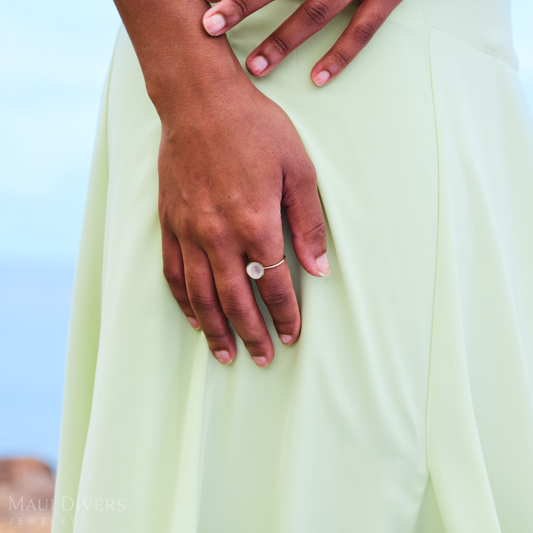 Close-up of a Cute Fruits Coconut Mother of Pearl Ring in 14k yellow gold worn on the index finger, with a pastel green dress visible in the background