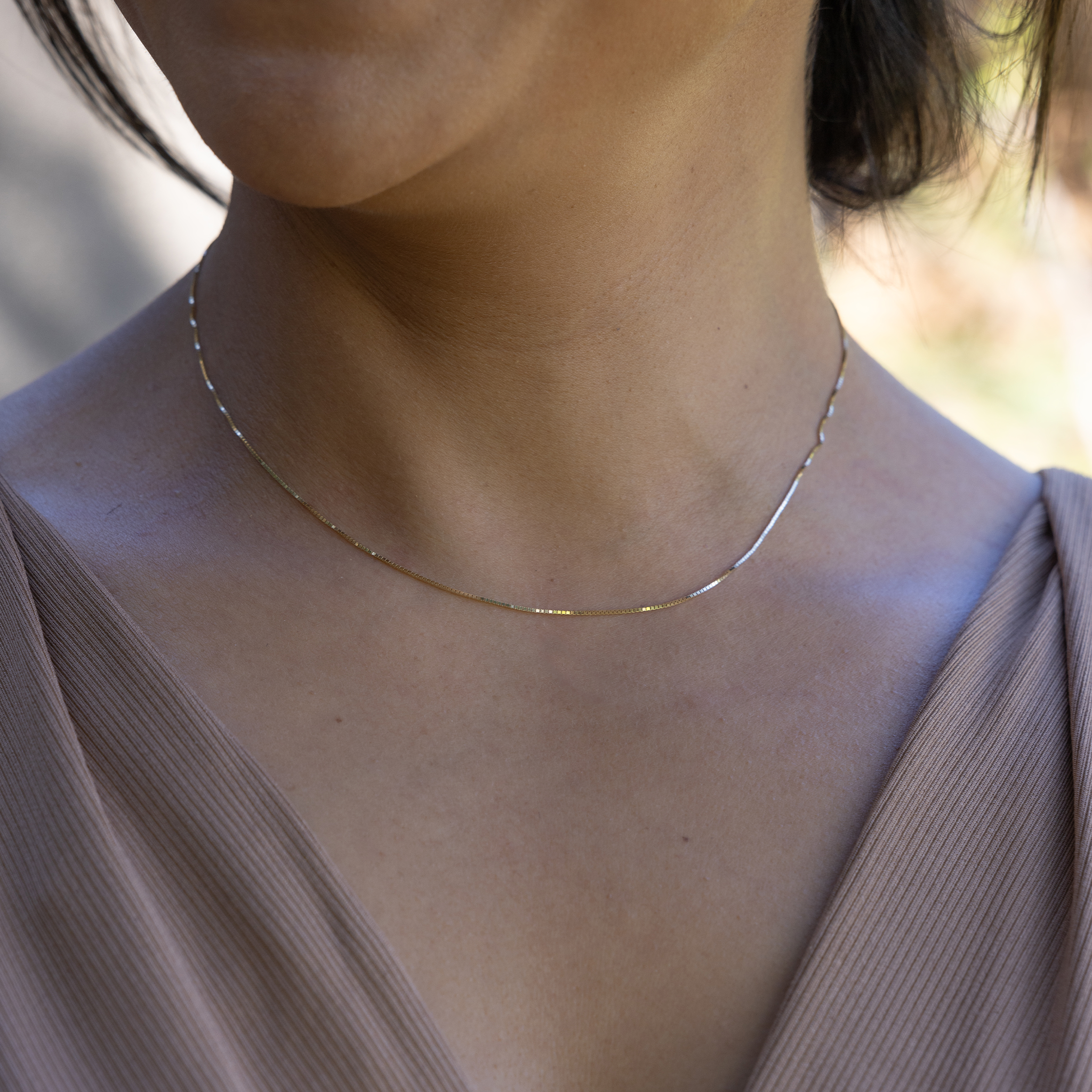 Close up of a woman wearing 0.8mm Venetian Box Chain in Gold outdoors