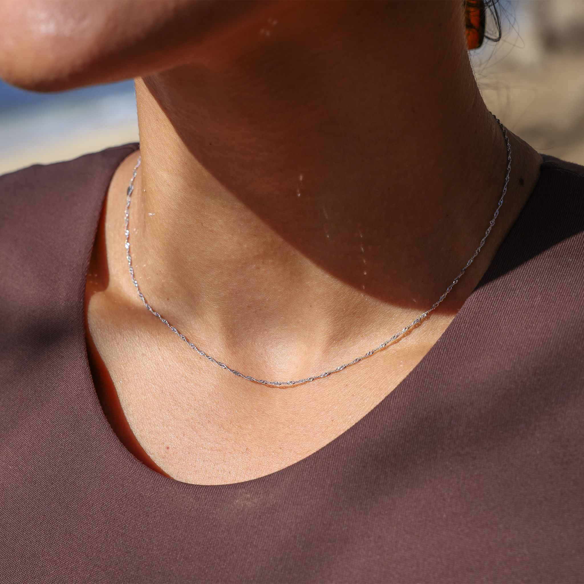 Close up of 1.0mm Singapore Chain in White Gold on a woman's neckline at the beach