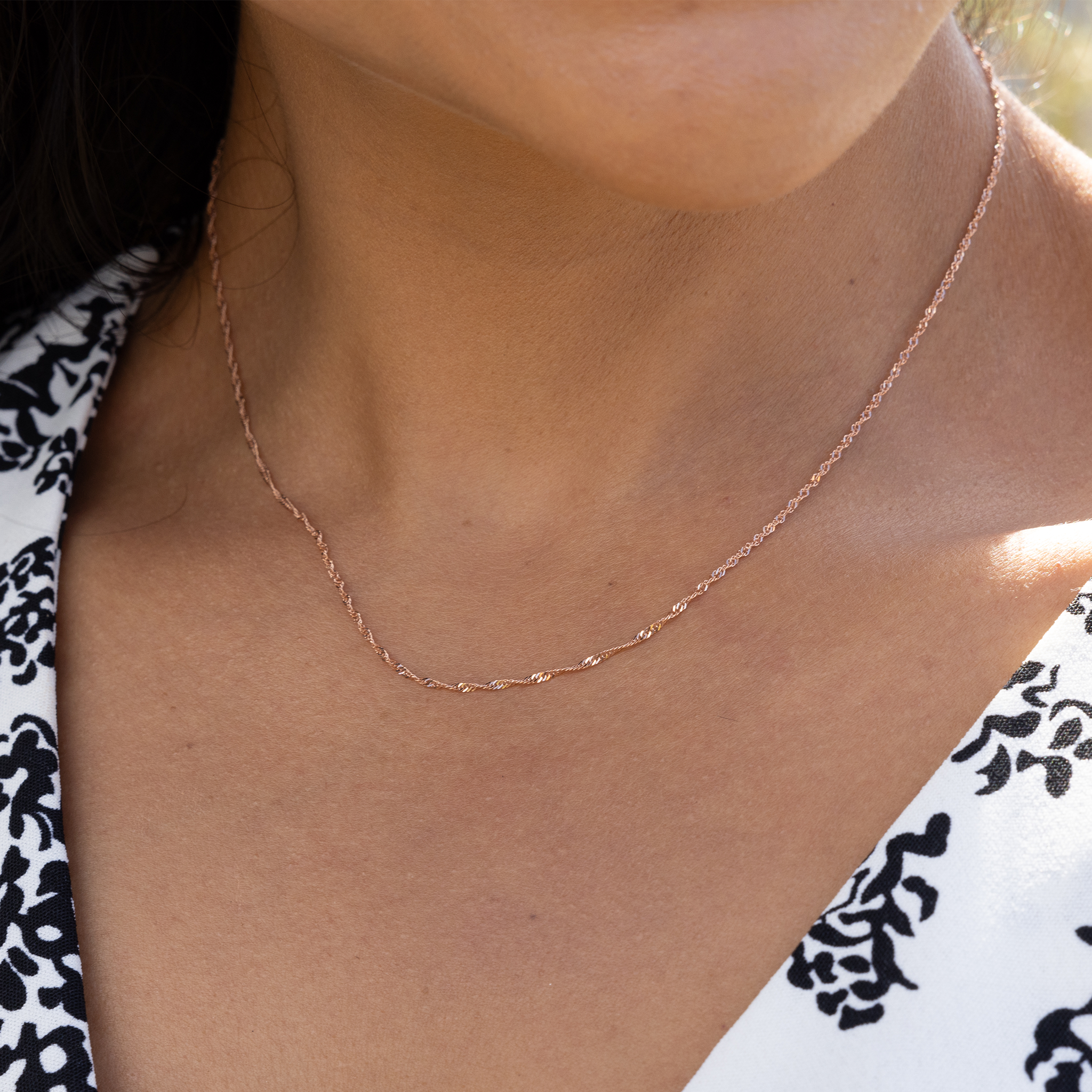 Close up of 1.0mm Singapore Chain in Rose Gold on woman's neckline outdoors