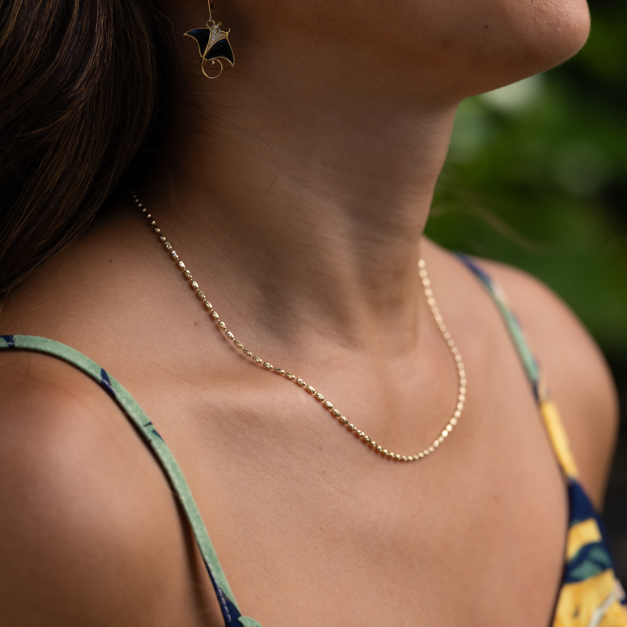 Close up of 1.8mm Ovalina Chain in Gold on woman's neckline with blurred green background
