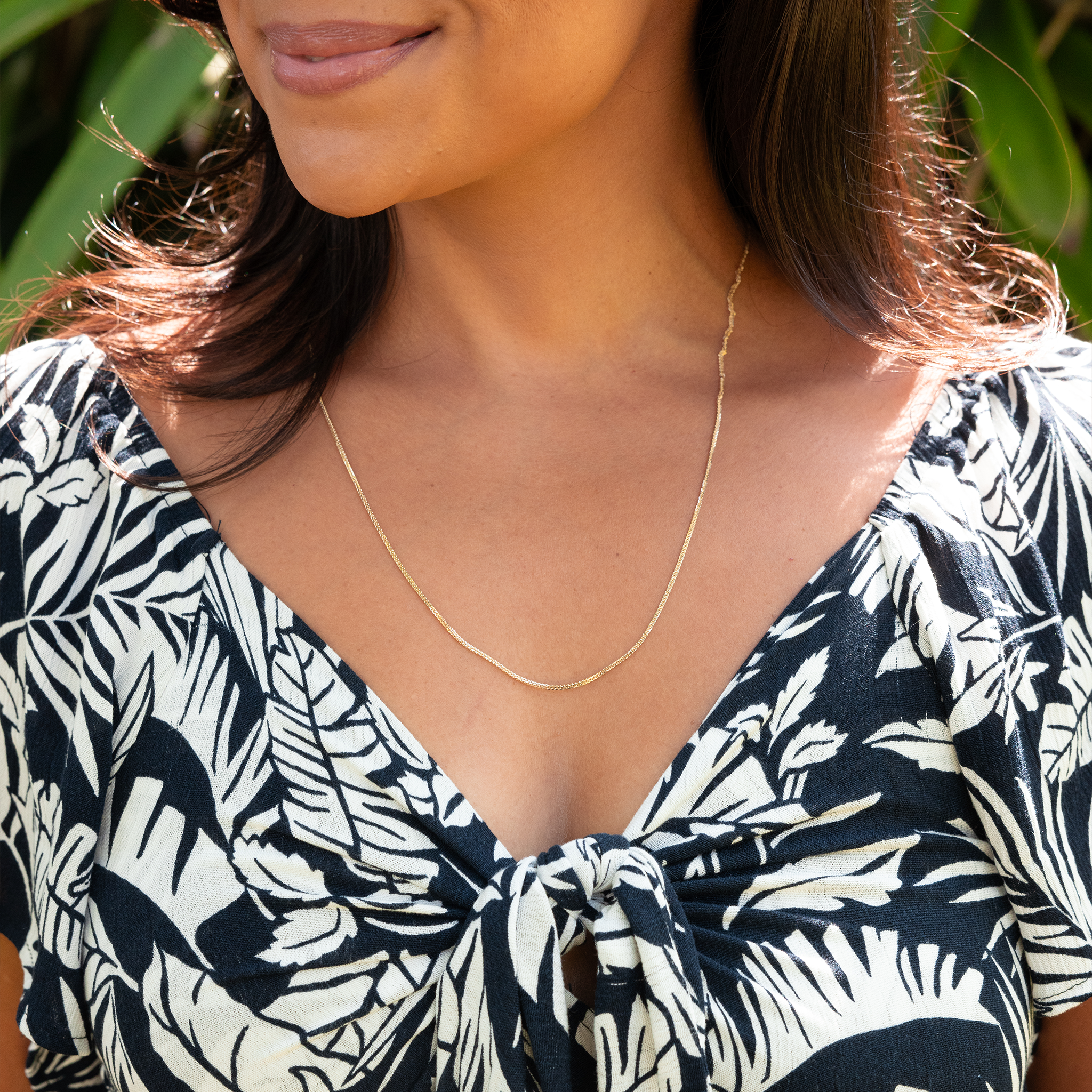 Woman in a garden wearing 1.4mm Espiga Chain in Gold with black and white pattern top