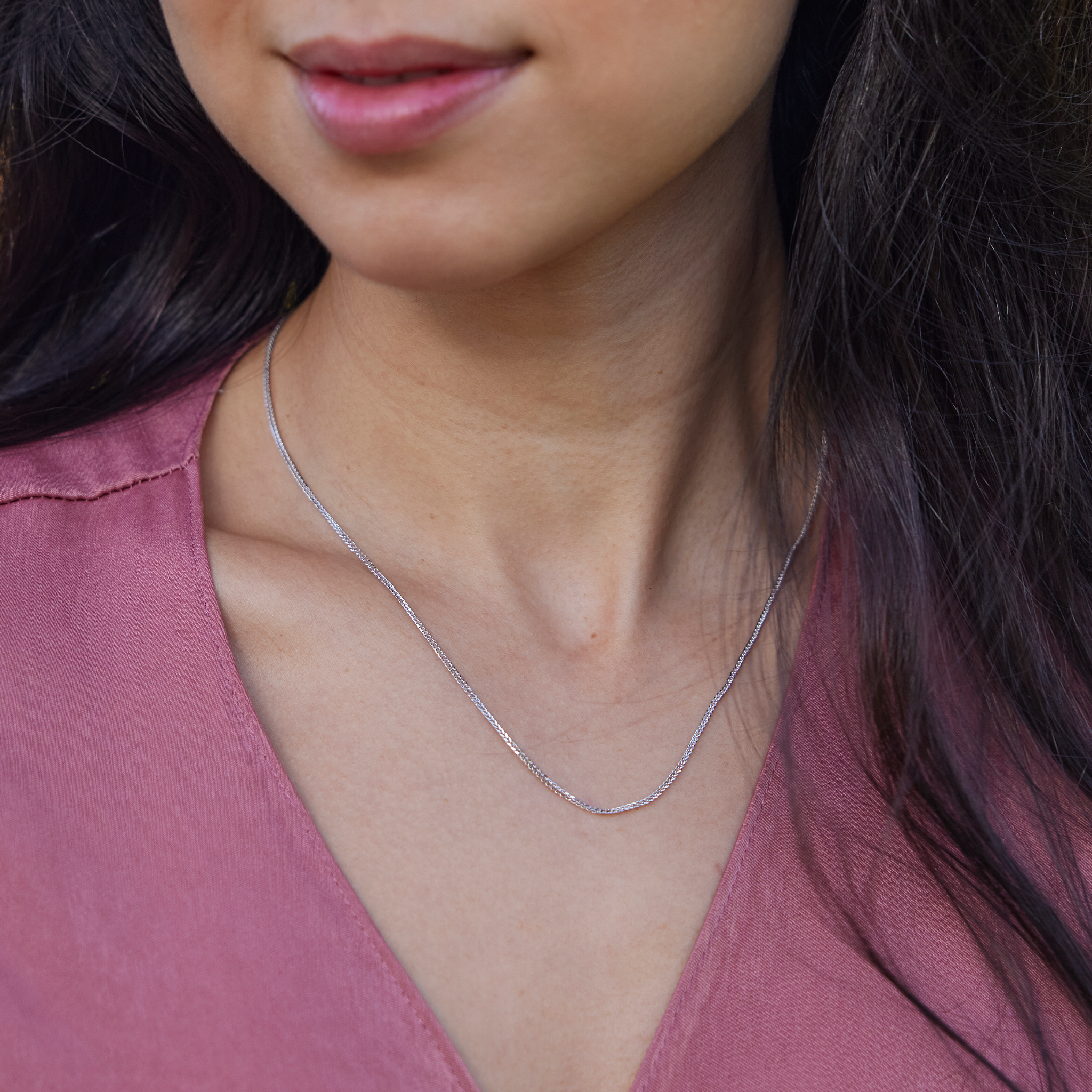Close up of 1.4mm Espiga Chain in White Gold on a woman's chest wearing a pink top