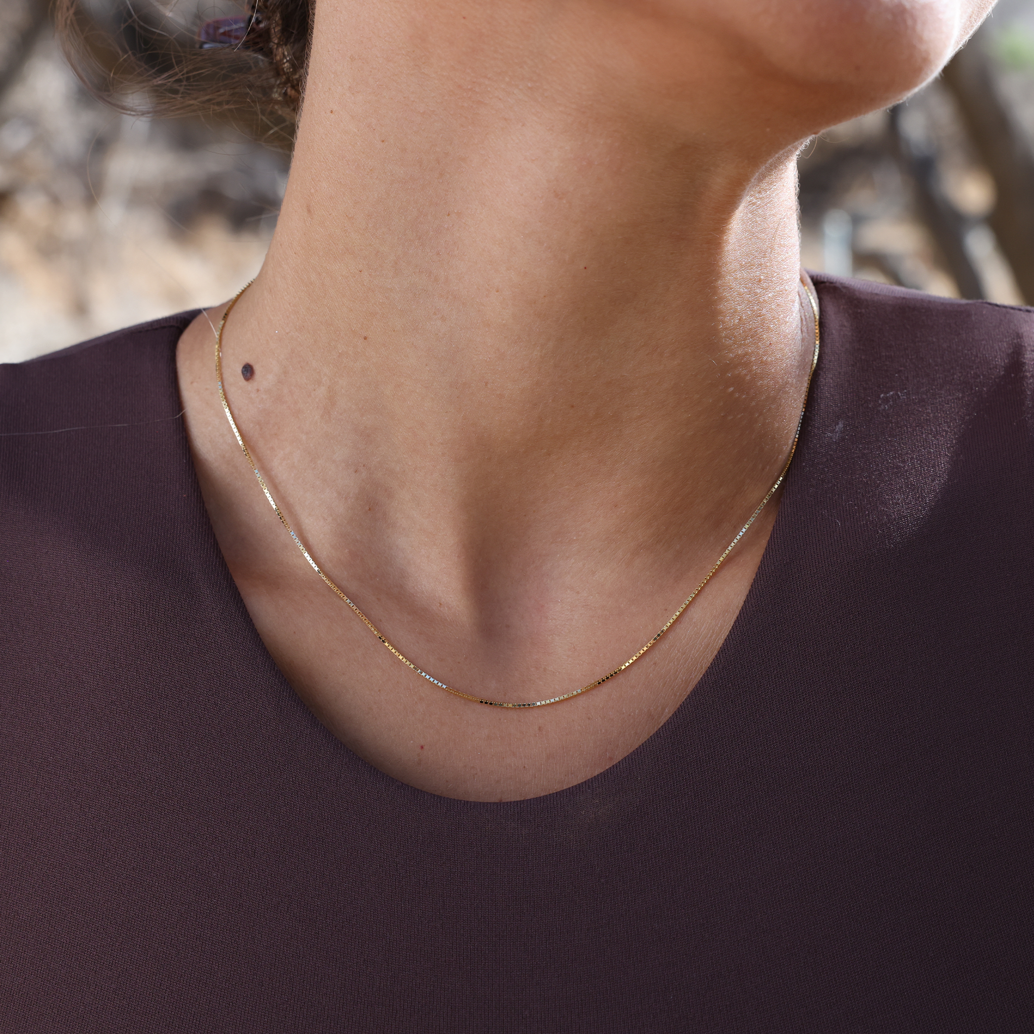 Close up of 0.85mm Box Chain in 14k Yellow Gold on a personʻs neckline