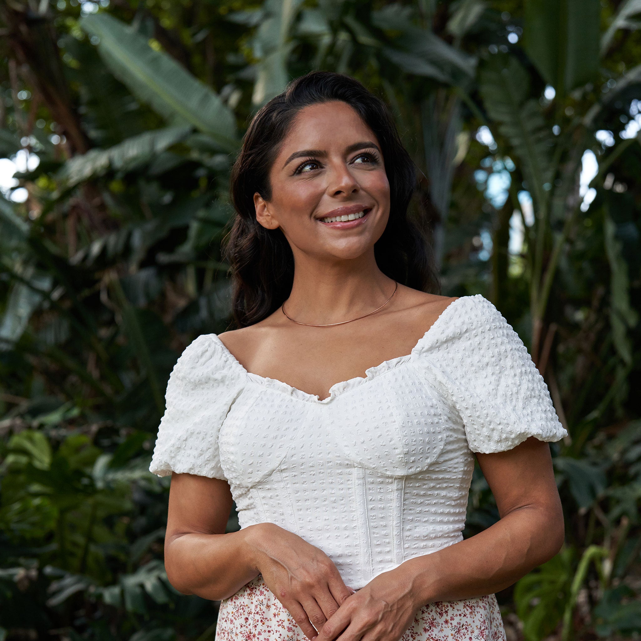 Woman in a tropical garden wearing a white top and 1.5mm Round Omega Chain in 14k Rose Gold