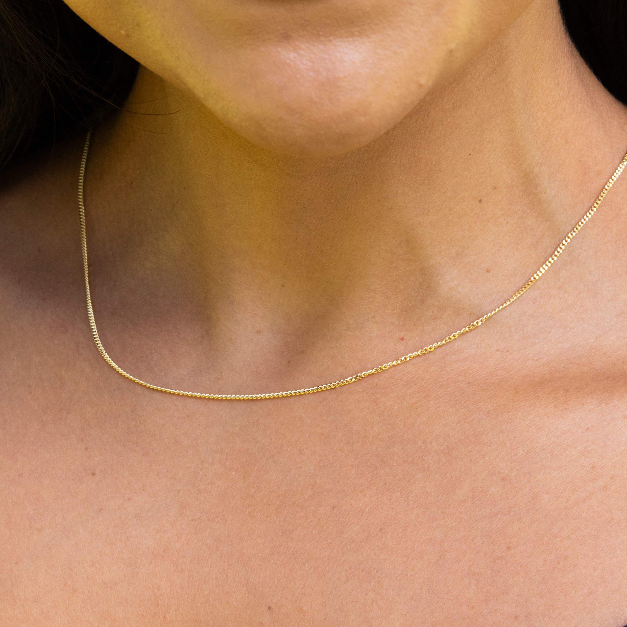 Close up of 1.5mm Gourmette Chain in 14k Yellow Gold on a personʻs neckline