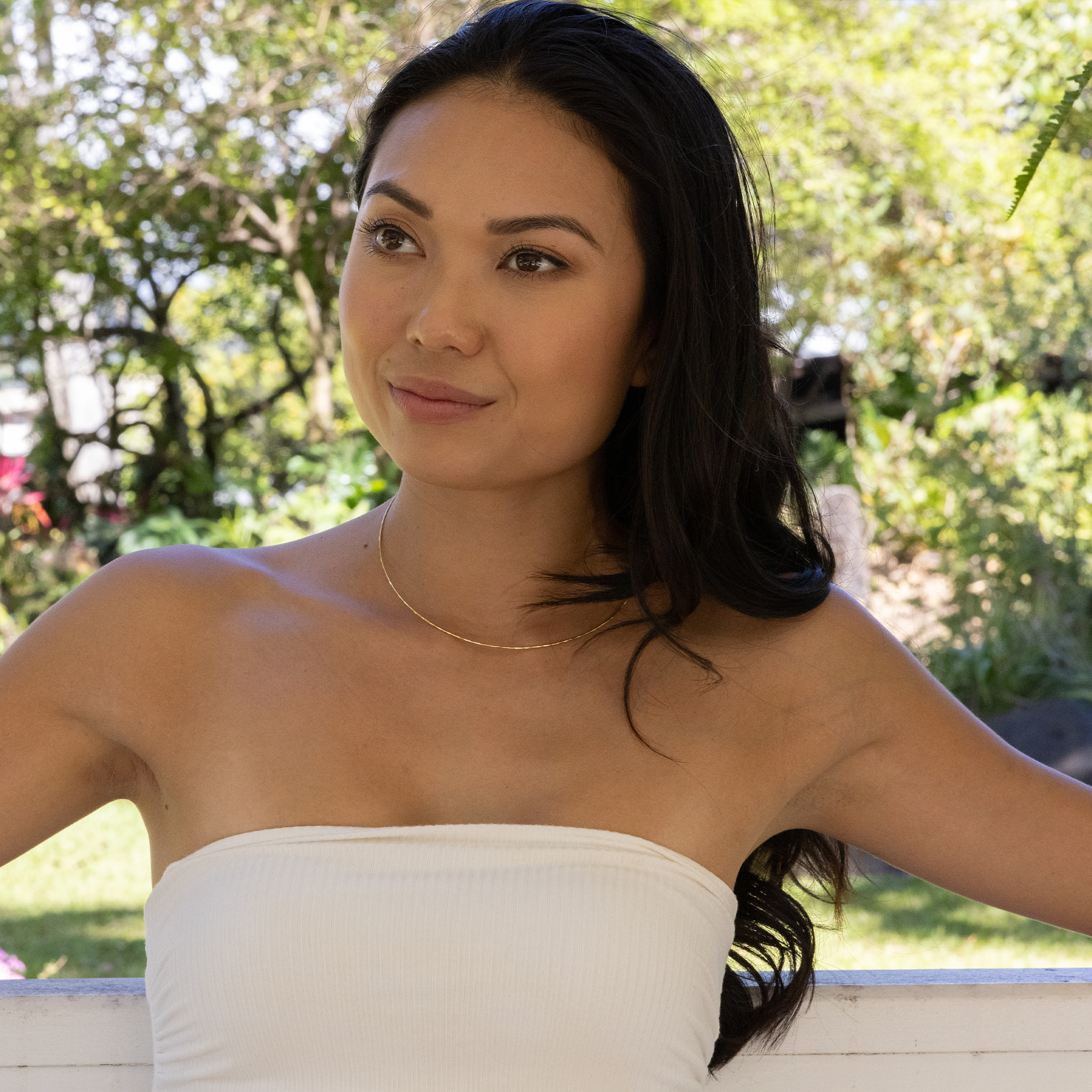 Woman in a garden wearing a white top and 1.5mm Round Omega Chain in 14k Yellow Gold
