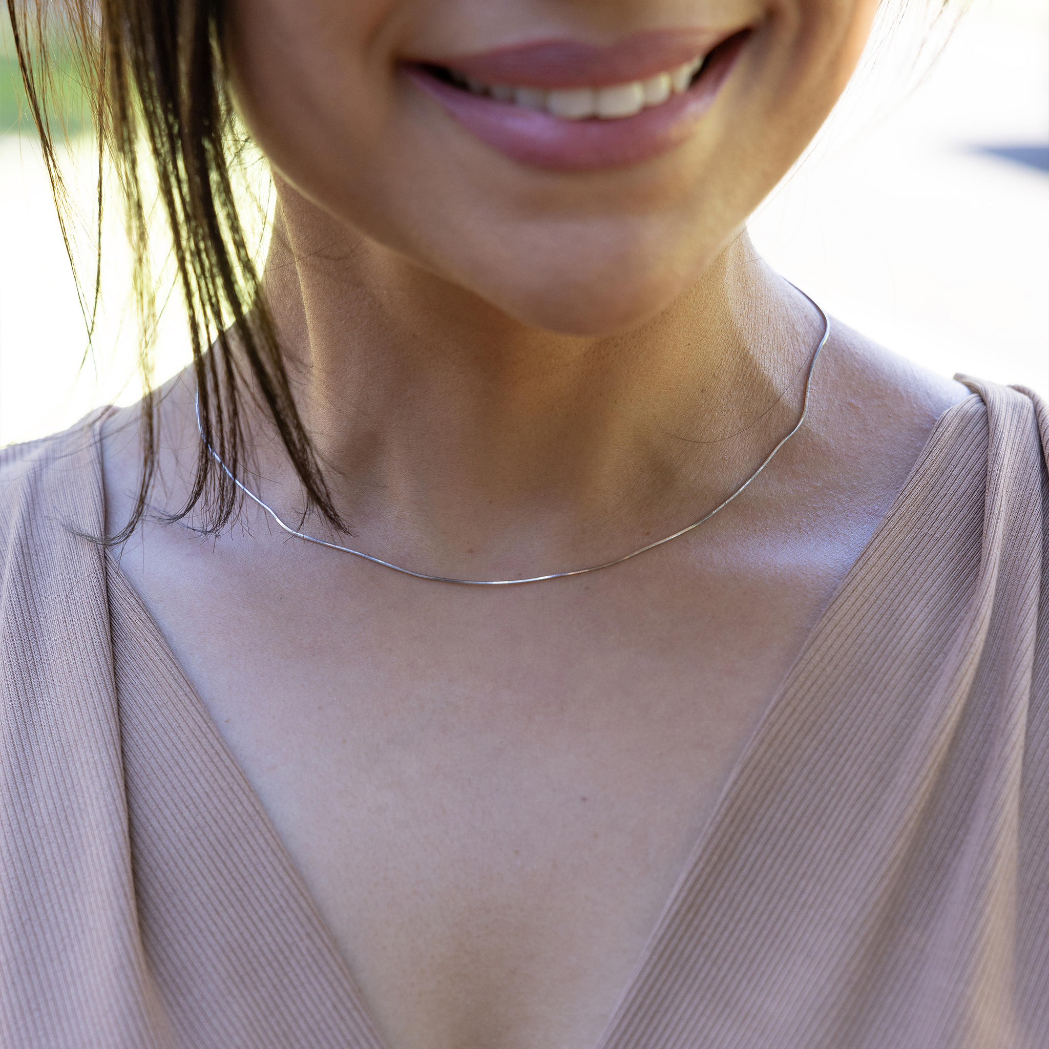 Close up of 1.0mm Snake Chain in Sterling Silver on a womanʻs neckline outdoors