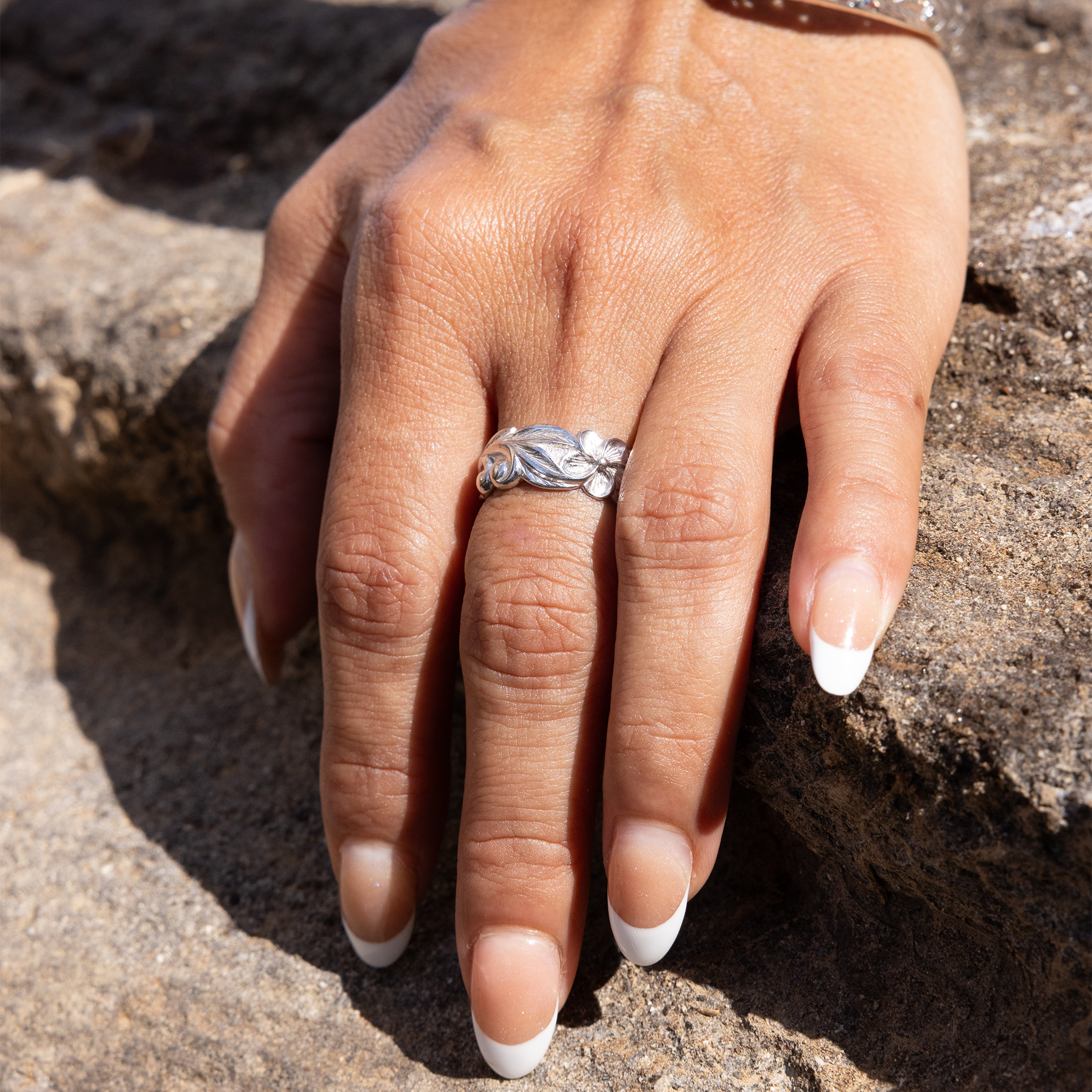 Womanʻs hand on a rock wearing Hawaiian Heirloom Plumeria Ring in Sterling Silver