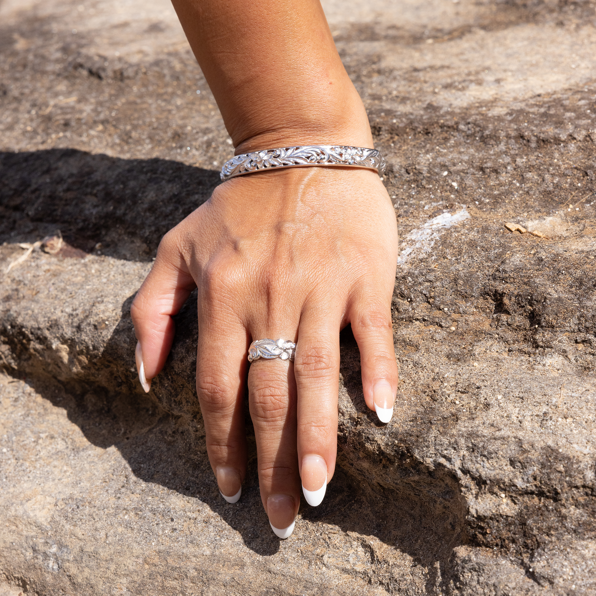 Womanʻs hand on a rock wearing Hawaiian Heirloom Plumeria Ring and bangle in Sterling Silver