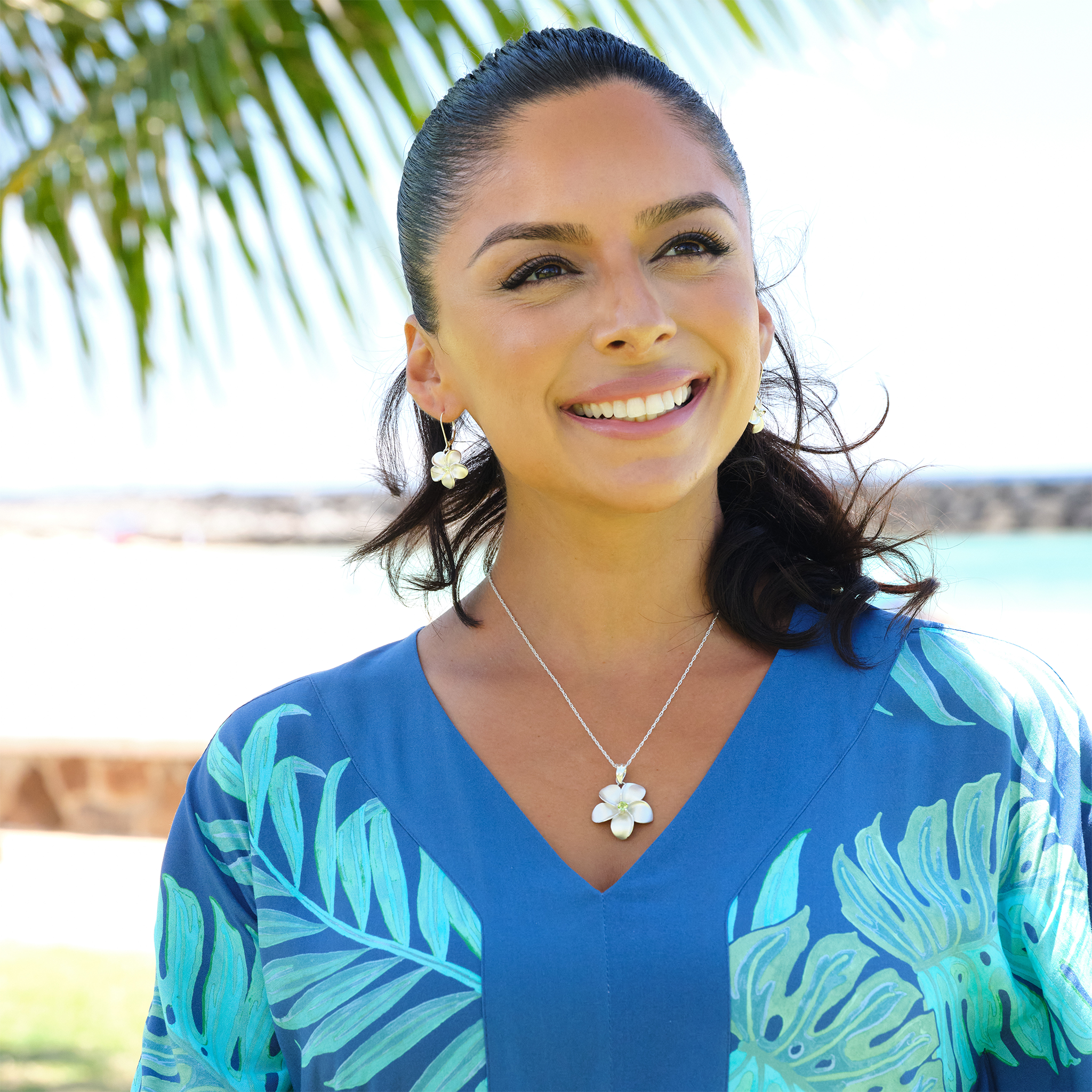 A woman on a beach wearing a Plumeria Peridot Earrings in Sterling Silver and blue floral dress