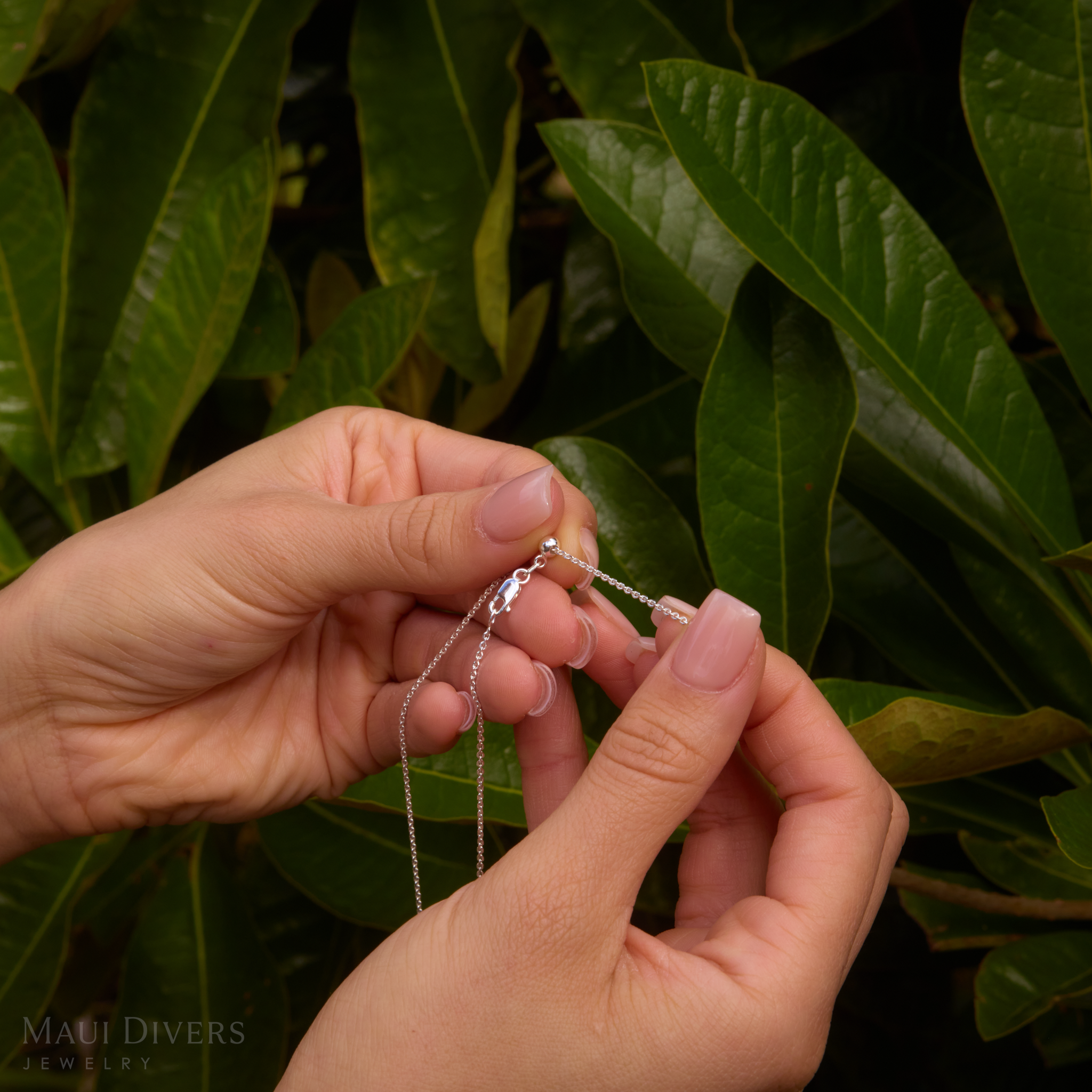 Hands showing adjustable detail on cable chain with green leaves in the background