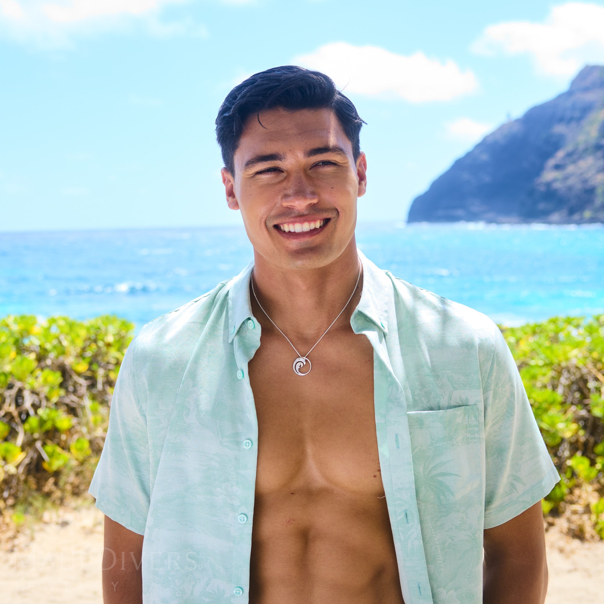 Man standing on a beach with clear blue sky wearing a Nalu Pendant Necklace in Sterling Silver
