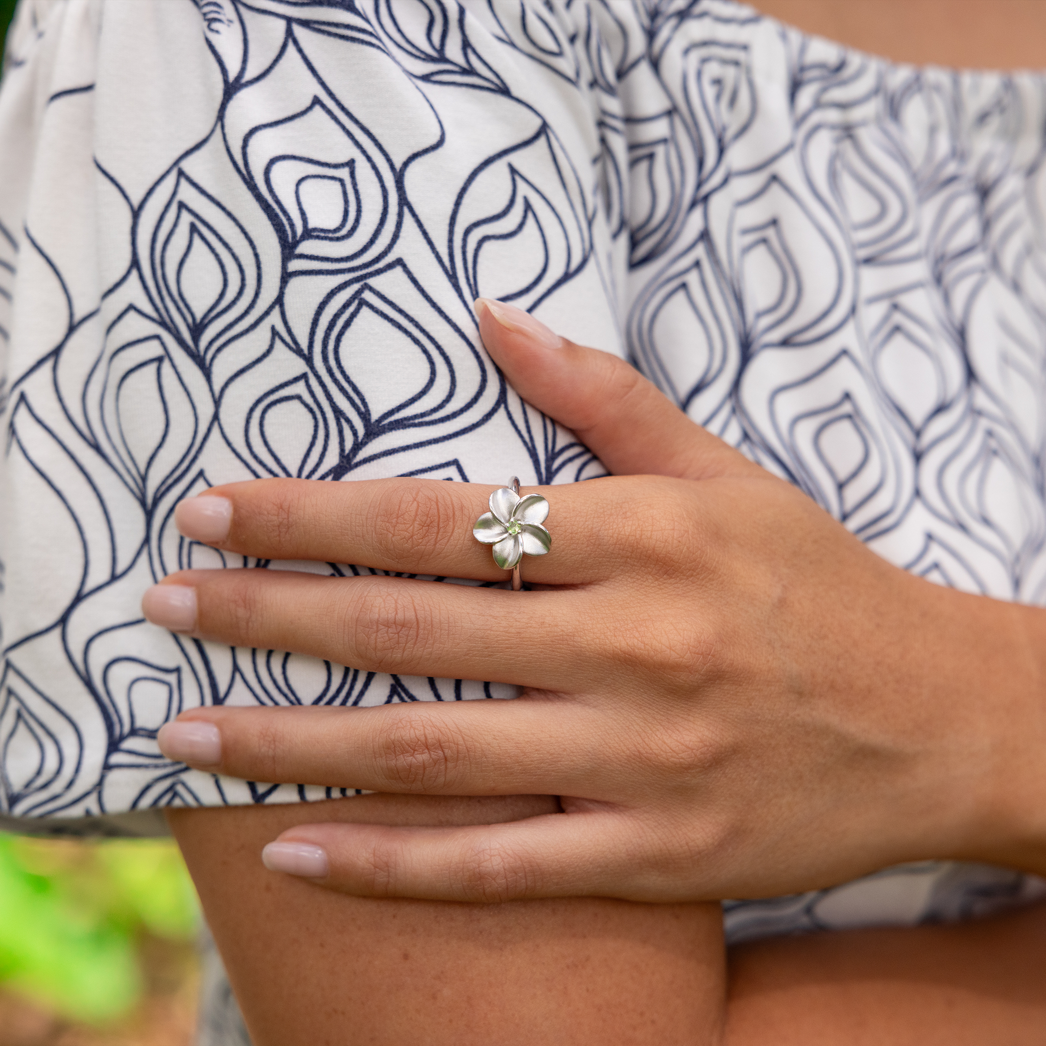 Close up of a Plumeria Peridot Ring in Sterling Silver on a woman's hand holding her arm