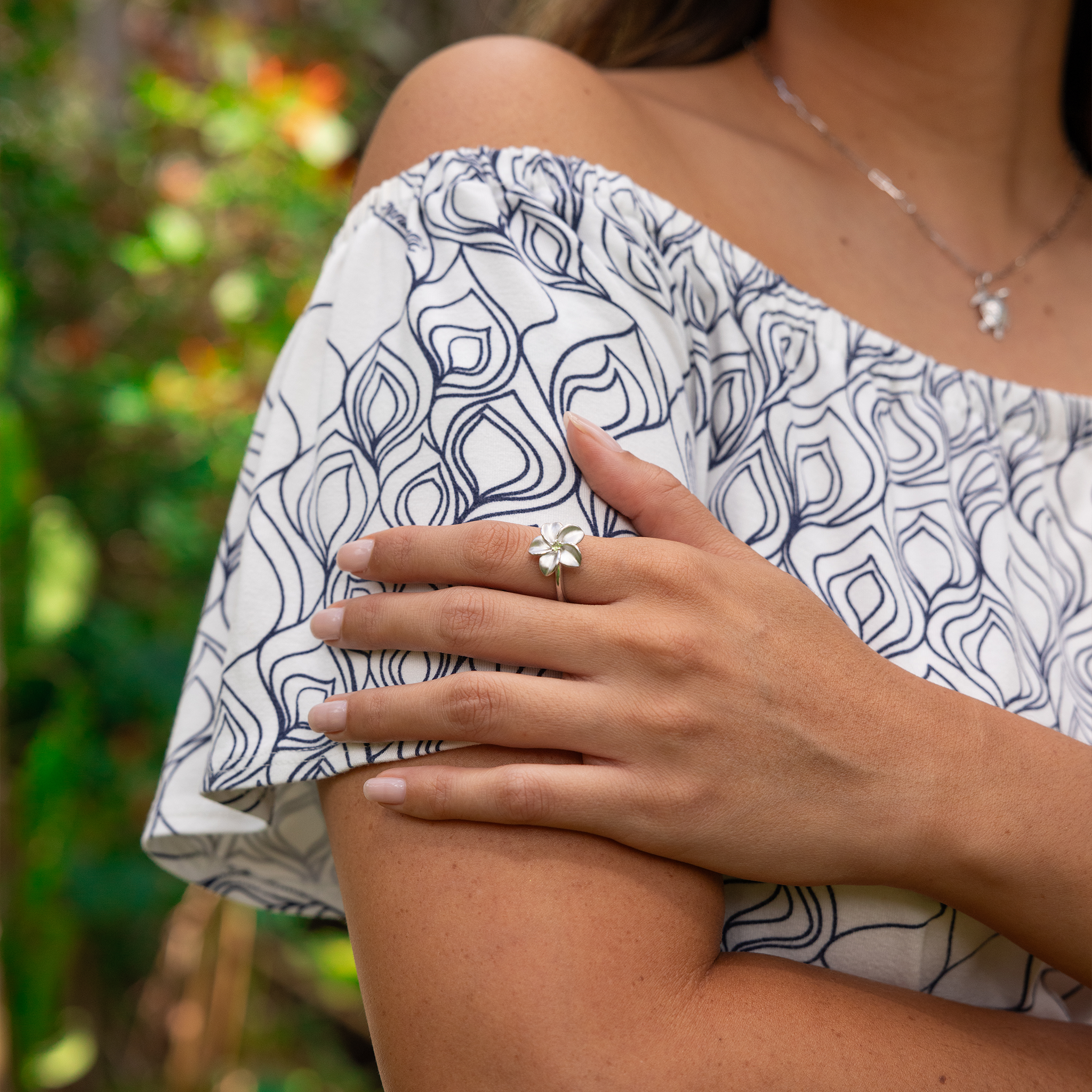 Woman holding her arm wearing a Plumeria Peridot Ring in Sterling Silver outdoors