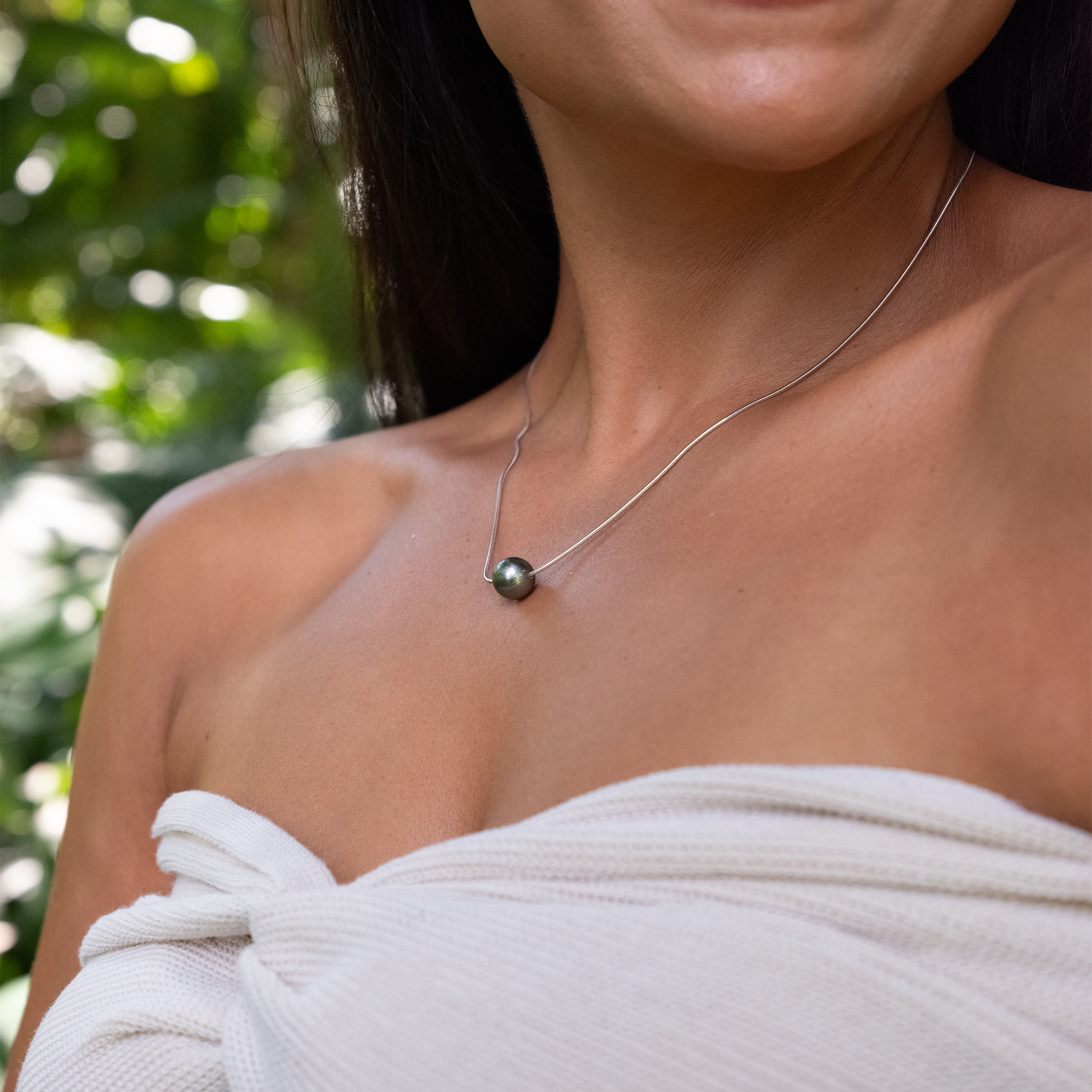 Close up of a Tahitian Black Pearl slider Necklace in Sterling Silver on a woman's chest outdoors