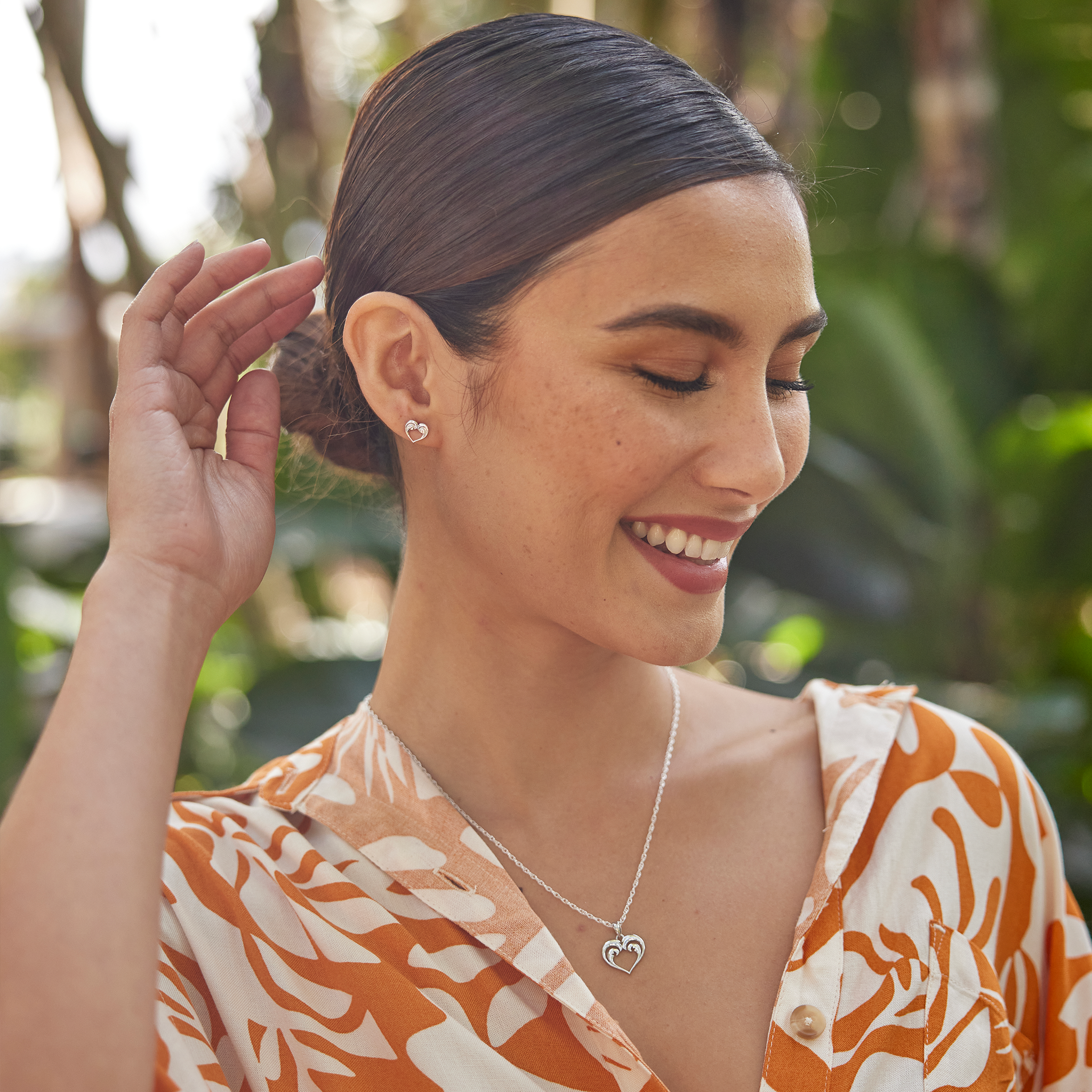 Woman in a garden wearing a Nalu Heart Necklace and earring in Sterling Silver