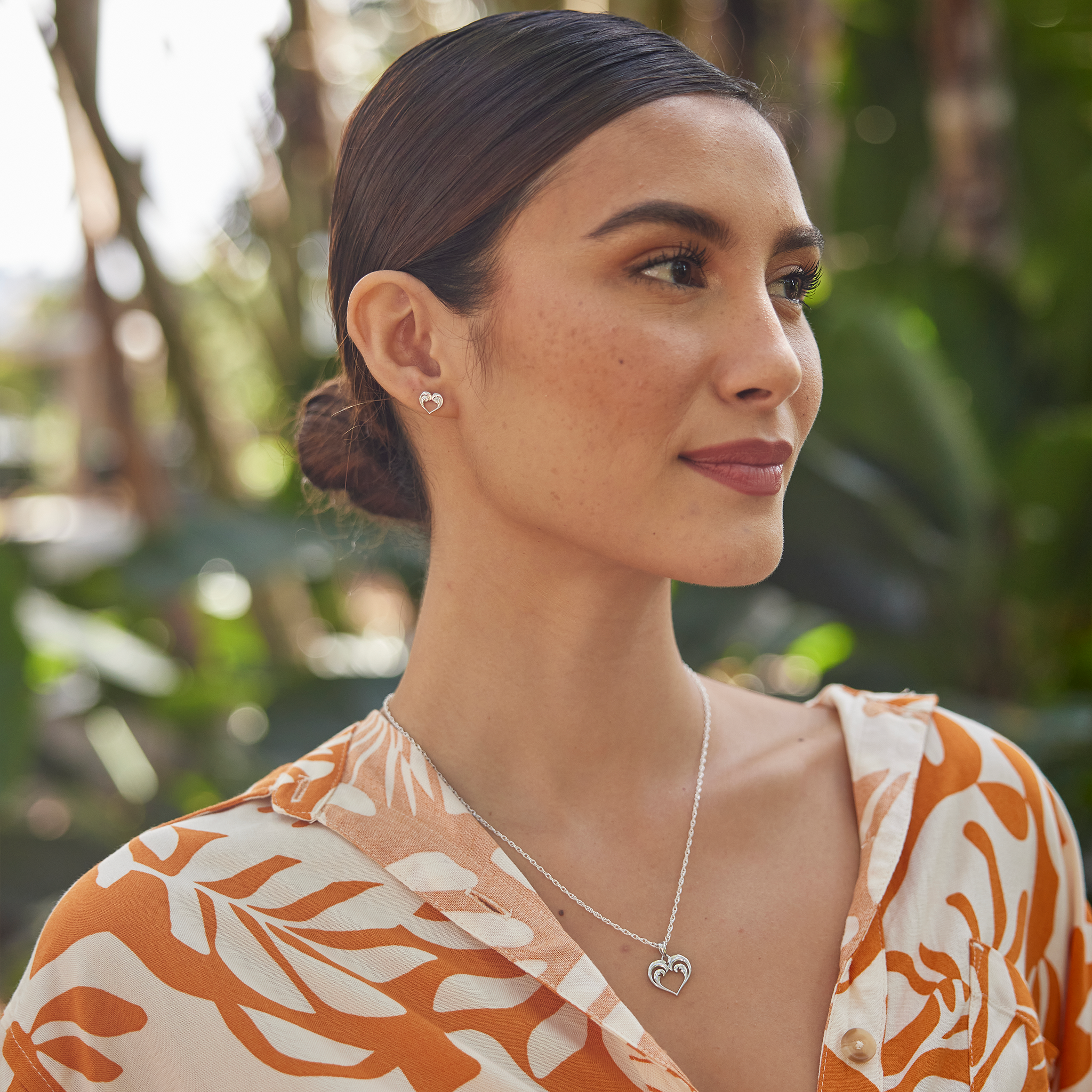 Woman in a garden wearing a Nalu Heart Necklace and earring in Sterling Silver