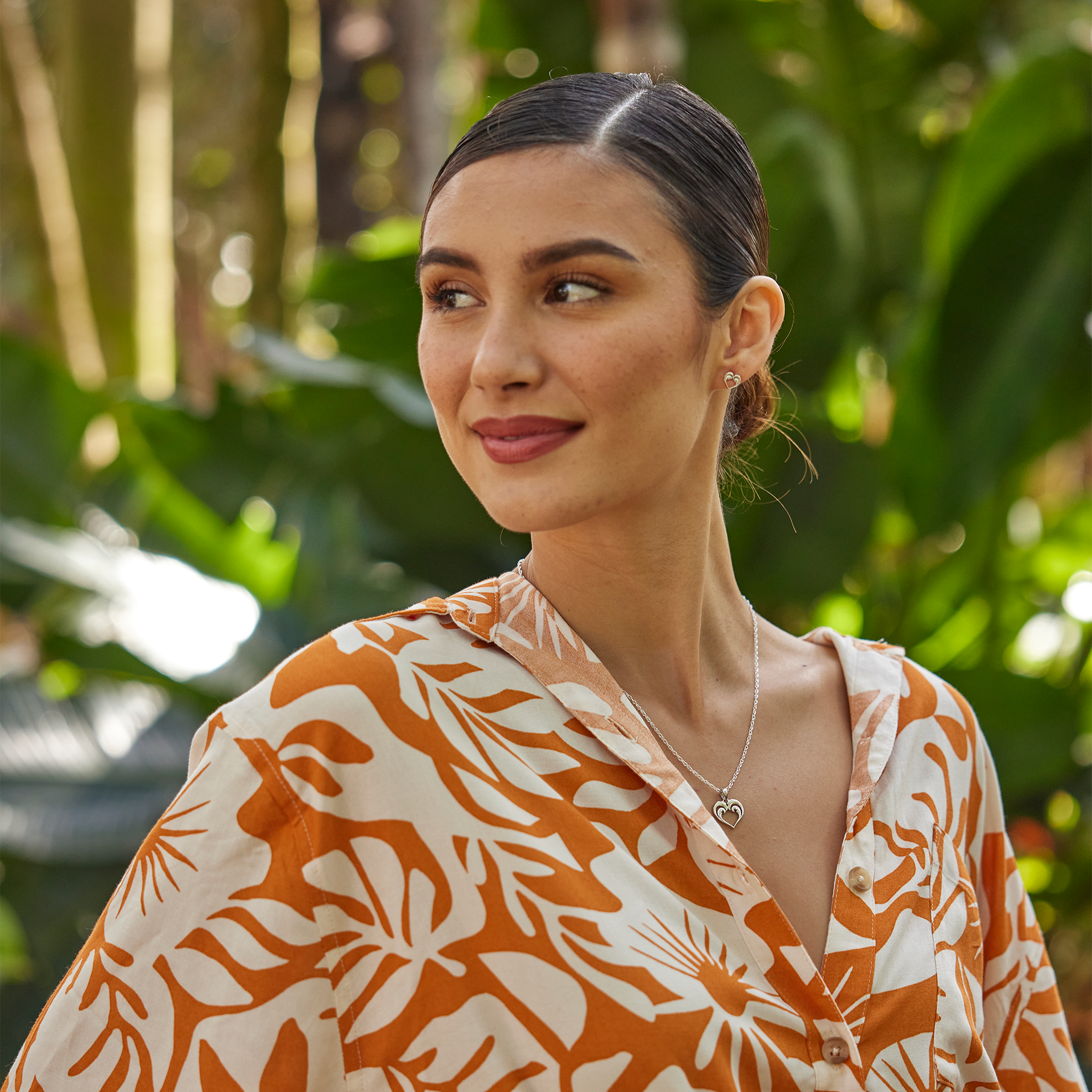 Woman in a garden wearing a Nalu Heart Necklace and earring in Sterling Silver