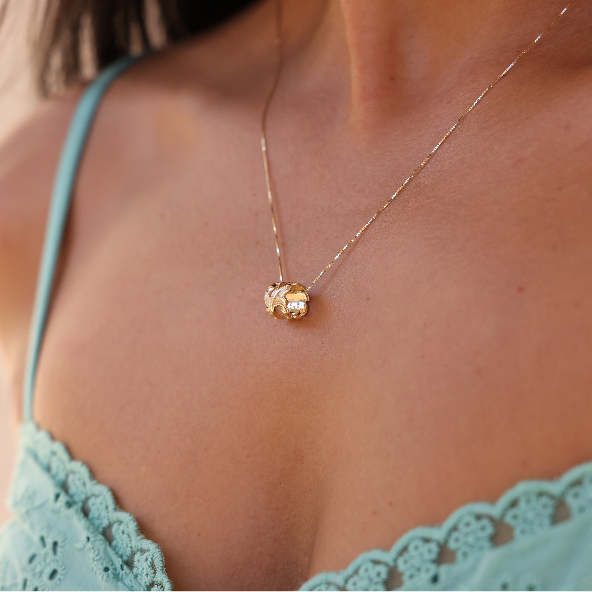 Hawaiian Heirloom Maile Scroll Barrel Pendant in Gold on Woman's Chest with Teal Top - Maui Divers Jewelry