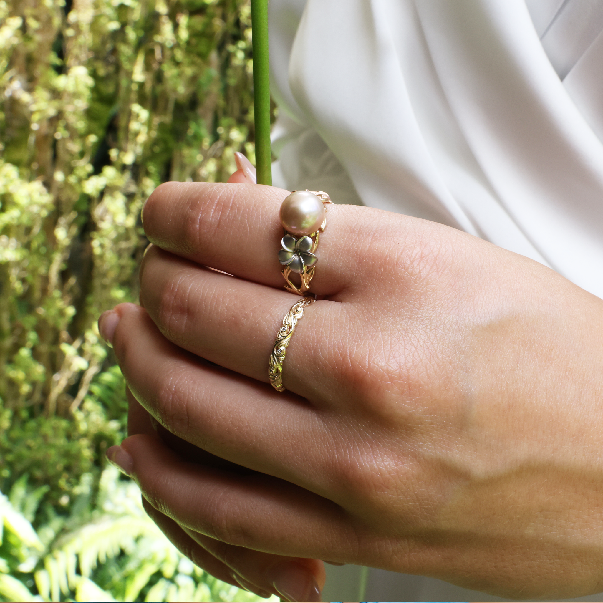 Close up of Living Heirloom Ring in Gold with Diamonds on woman's hand with blurred greenery in back