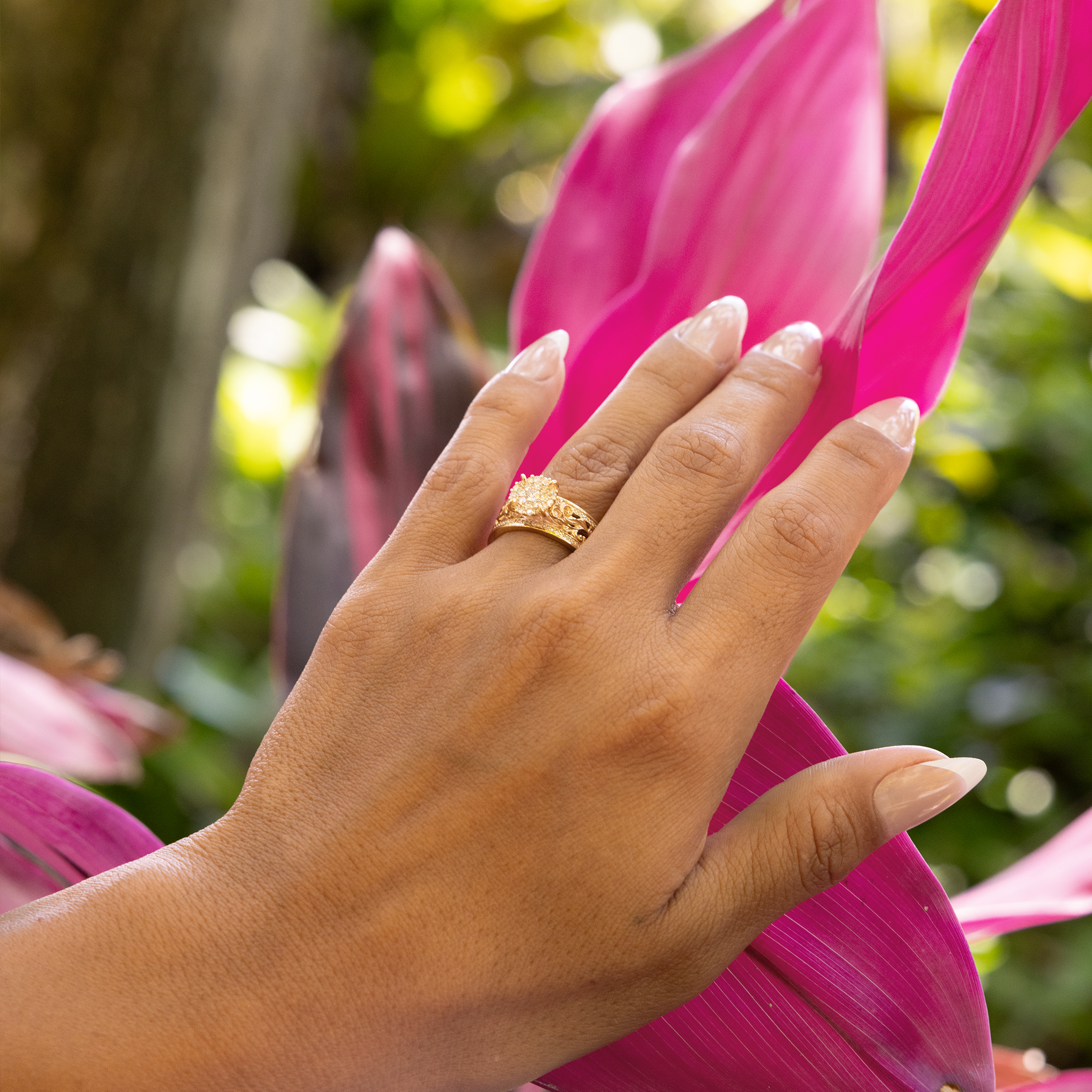 Living Heirloom Engagement Ring in Gold with Diamonds on a woman's hand against a pink leafy plant