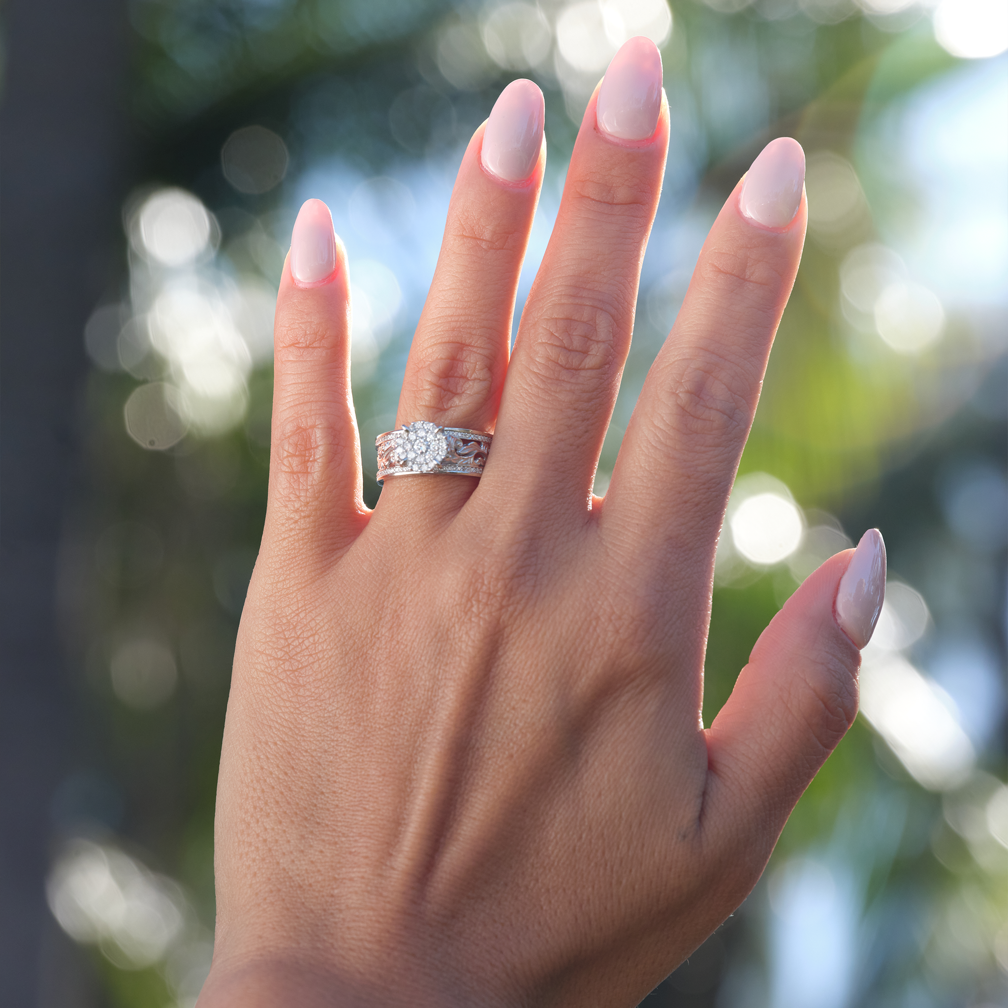 Woman's hand with a Hawaiian Heirloom Engagement Ring in White Gold with Diamonds and blurred trees in background