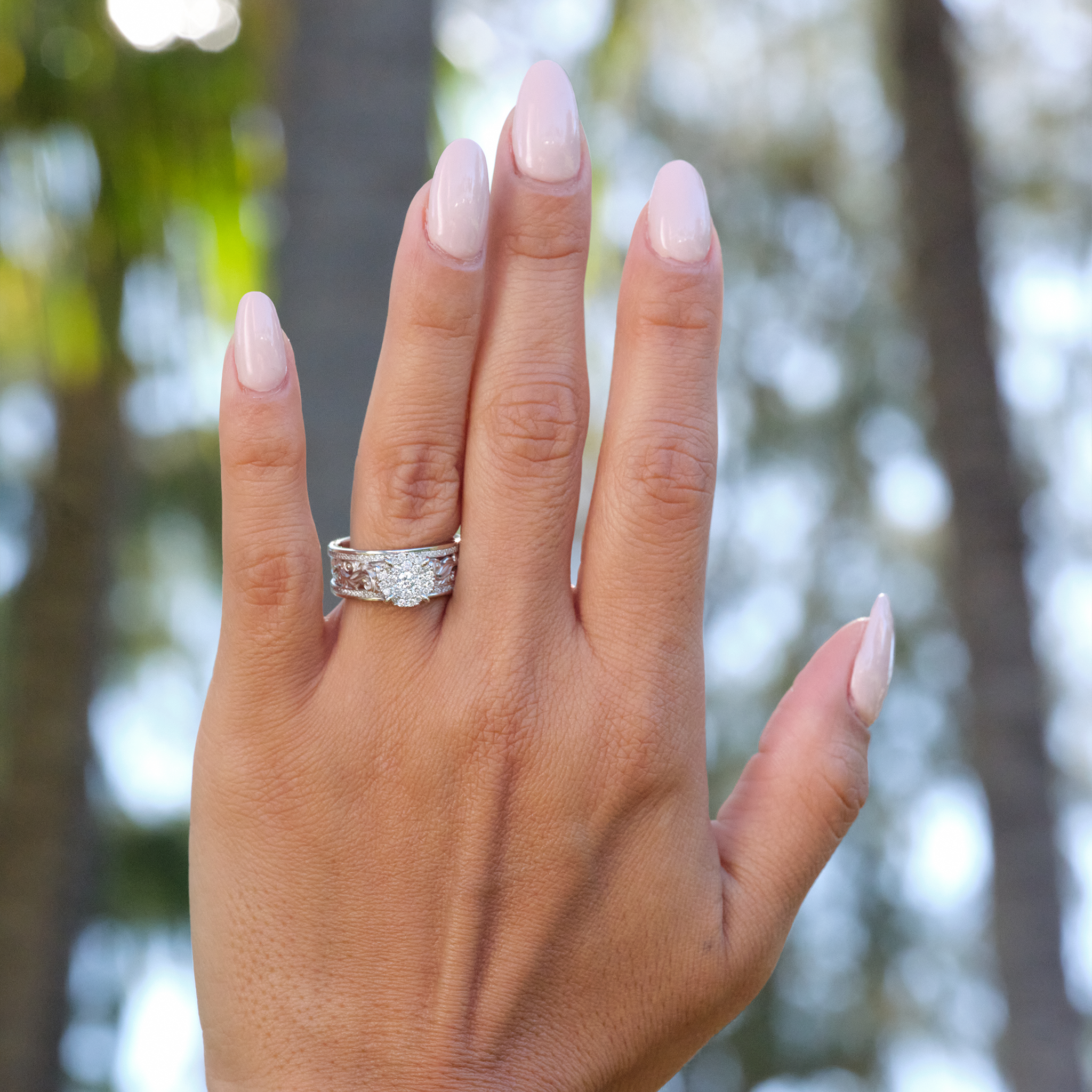 Woman's hand with a Hawaiian Heirloom Engagement Ring in White Gold with Diamonds and blurred trees in background