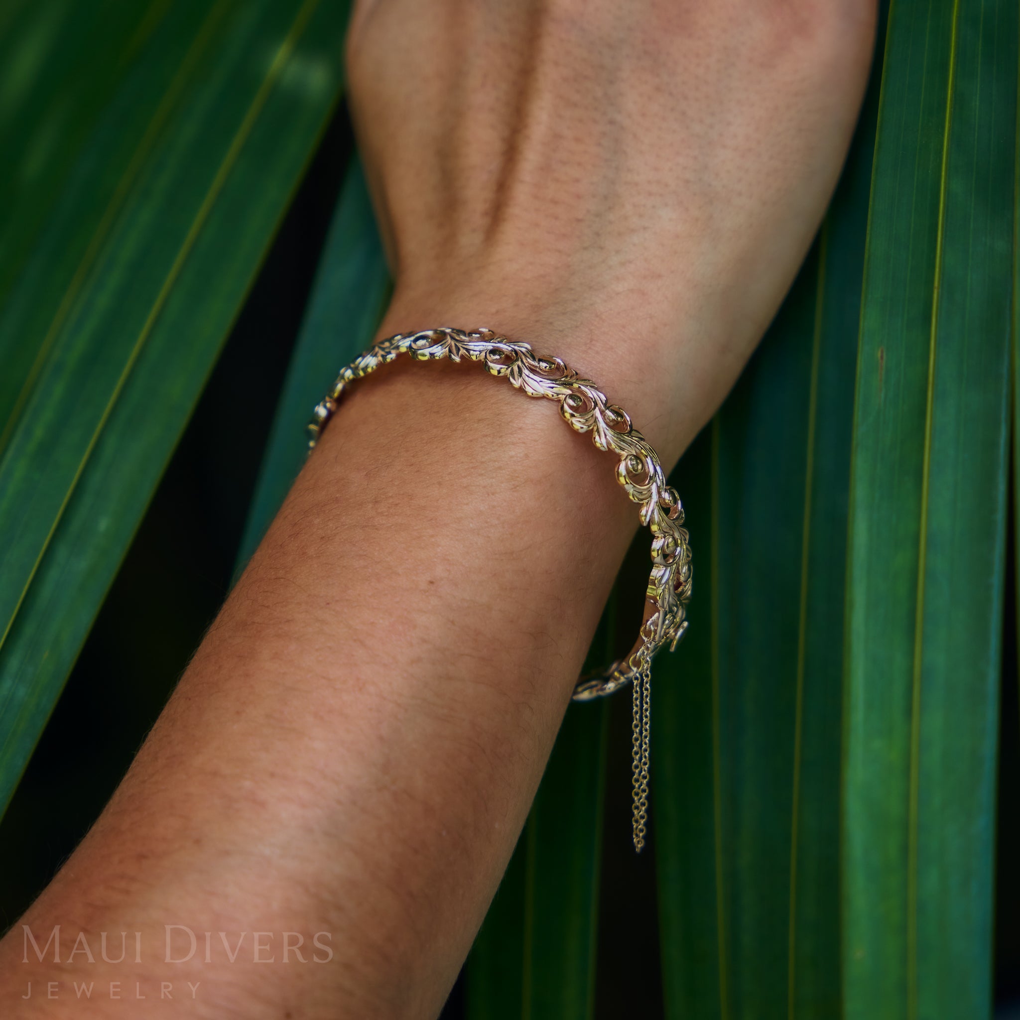 Close-up of a Living Heirloom Hinge Bracelet in 14k Yellow Gold on a wrist with a green leafy background