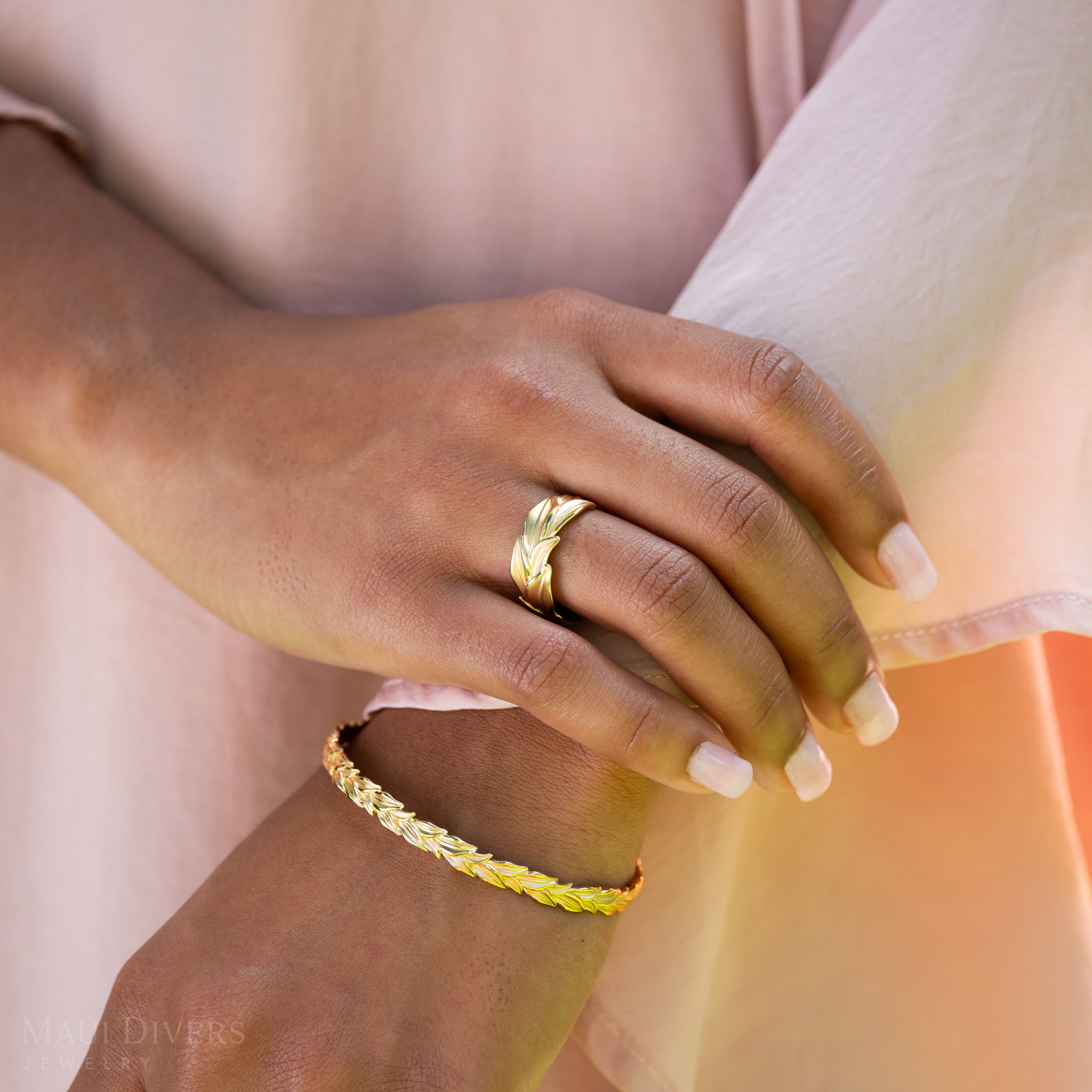 Close-up of a hand wearing a 10mm Maile Ring in Gold and bracelet against a blurred background