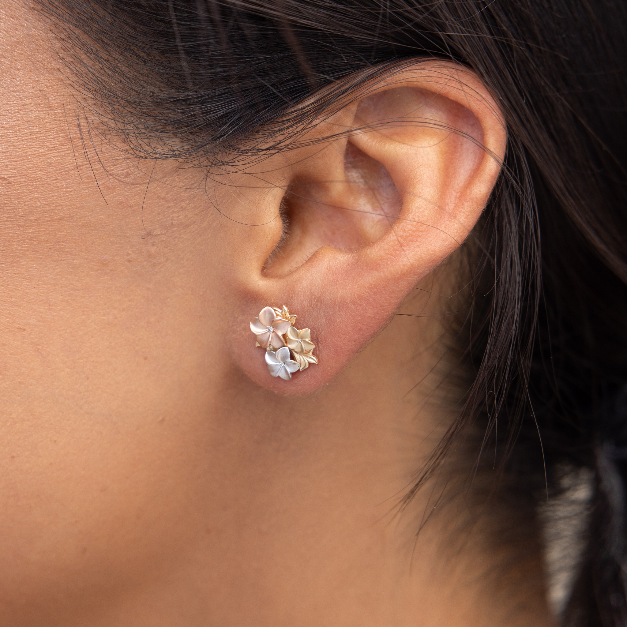 Close up of Plumeria Earrings in Tri Color Gold with Diamonds on ear