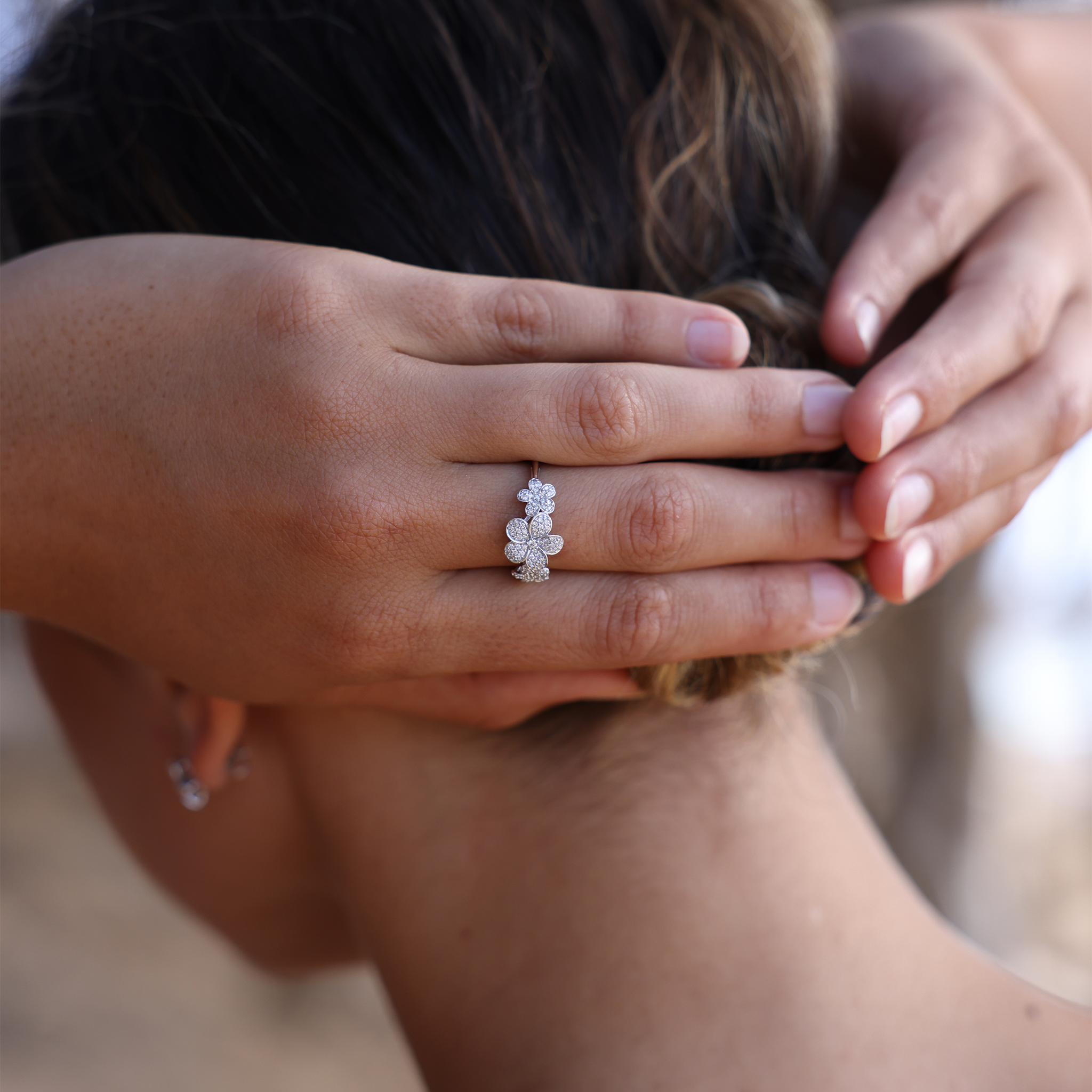 Close up of 10mm Three Plumeria Ring in White Gold with Diamonds on hands holding up hair