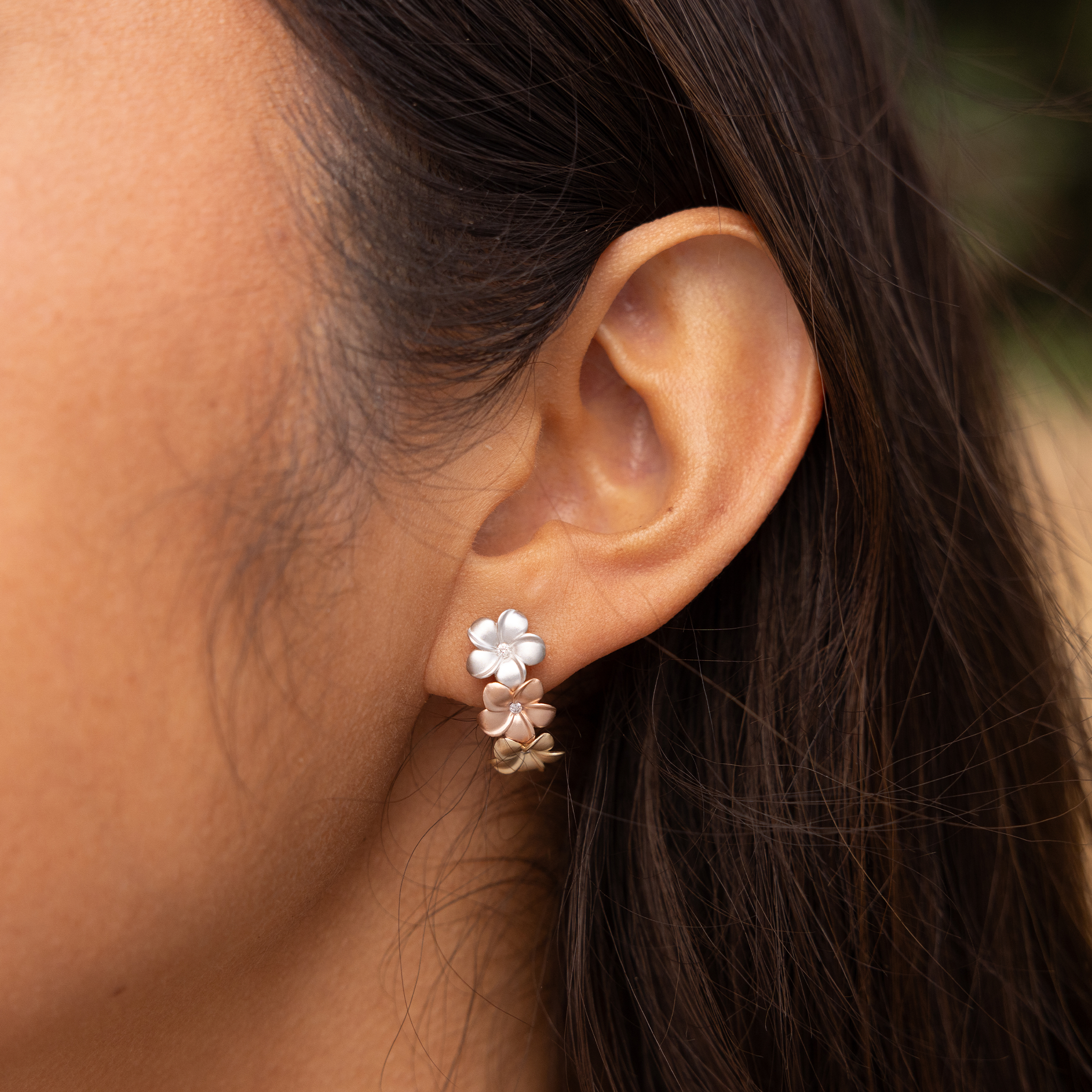 Close up of Plumeria Earrings in Tri Color Gold with Diamonds on ear