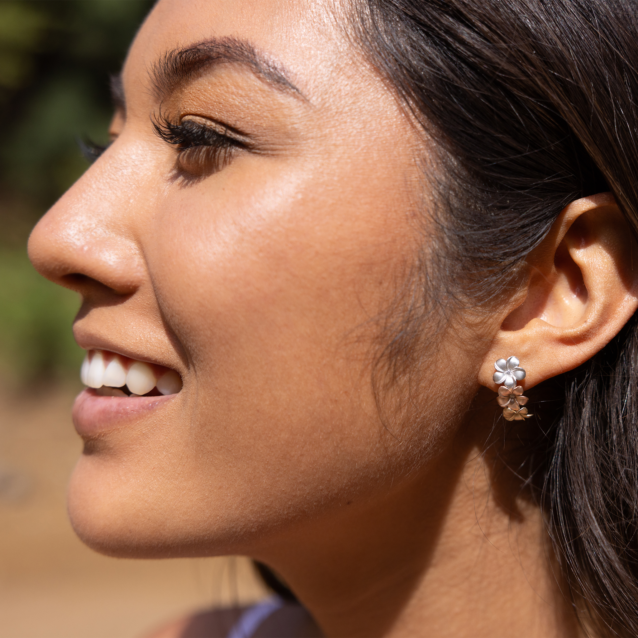 Close up of woman wearing Plumeria Earrings in Tri Color Gold with Diamonds outdoors